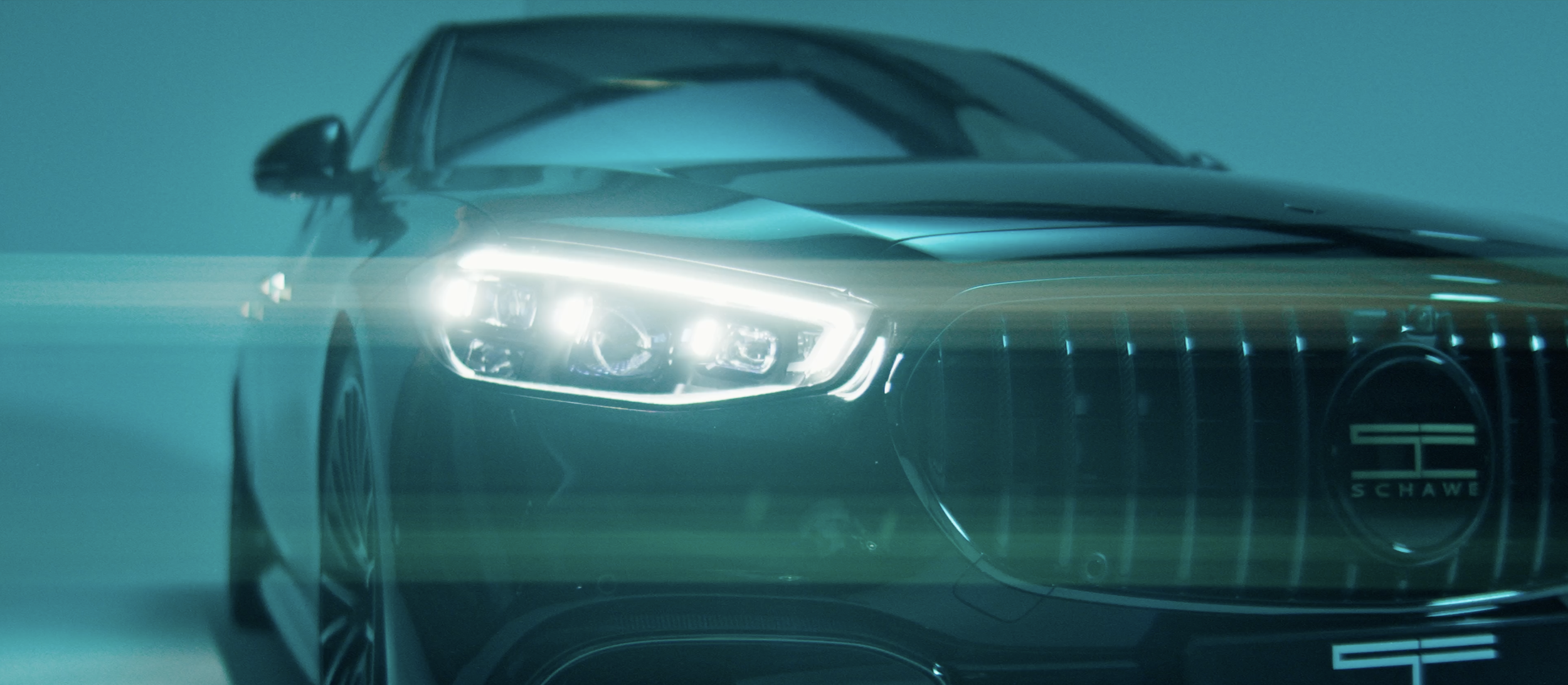 Dunkler, moderner Mercedes-Benz mit leuchtenden Scheinwerfern, teilweise sichtbar, im Dunkeln mit bläulichem Licht. Das Auto ist dynamisch ins Bild gesetzt.