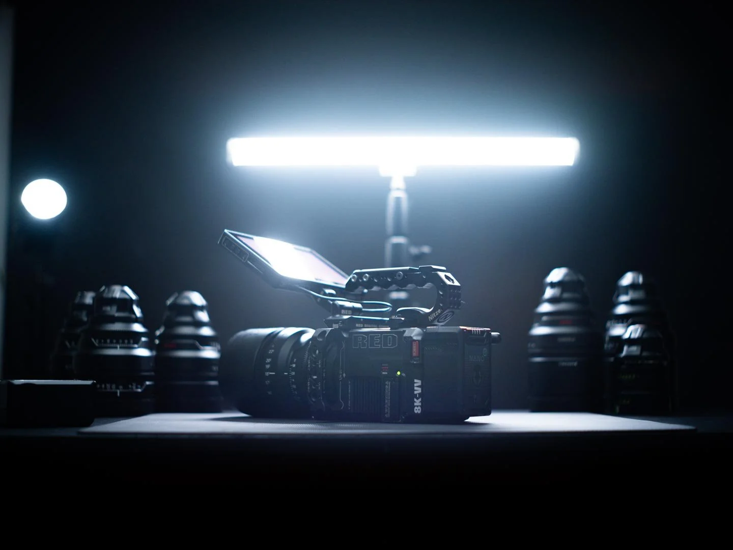 Eine Red V-Raptor VV mit Kamerahalterung auf einem Tisch, umgeben von mehreren Objektiven, beleuchtet von einem hellen Lichtstrahl im Dunkeln.