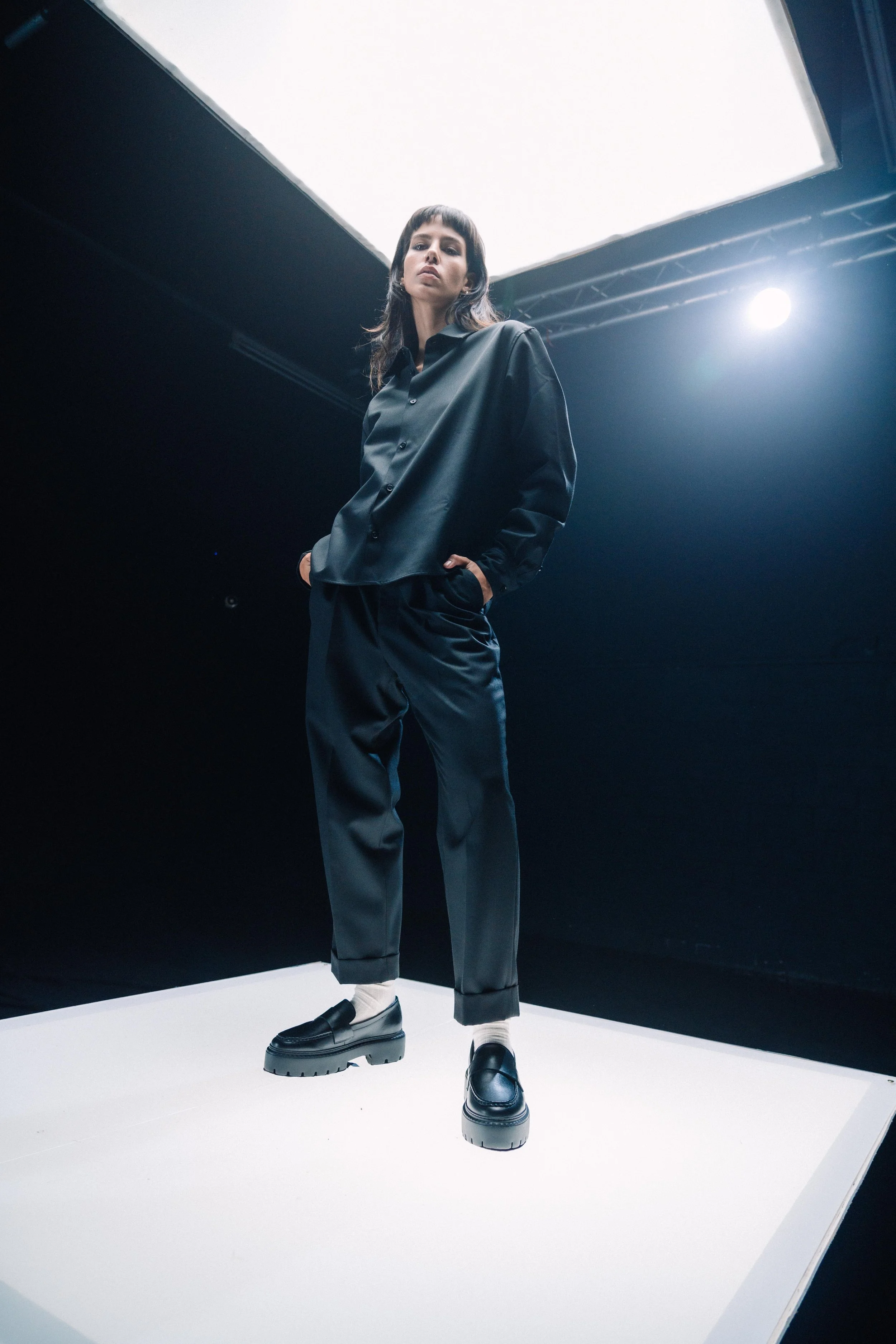 Eine Frau steht auf einer weißen Plattform in einem dunklen Raum mit einer hellen, unteren Lichtquelle.