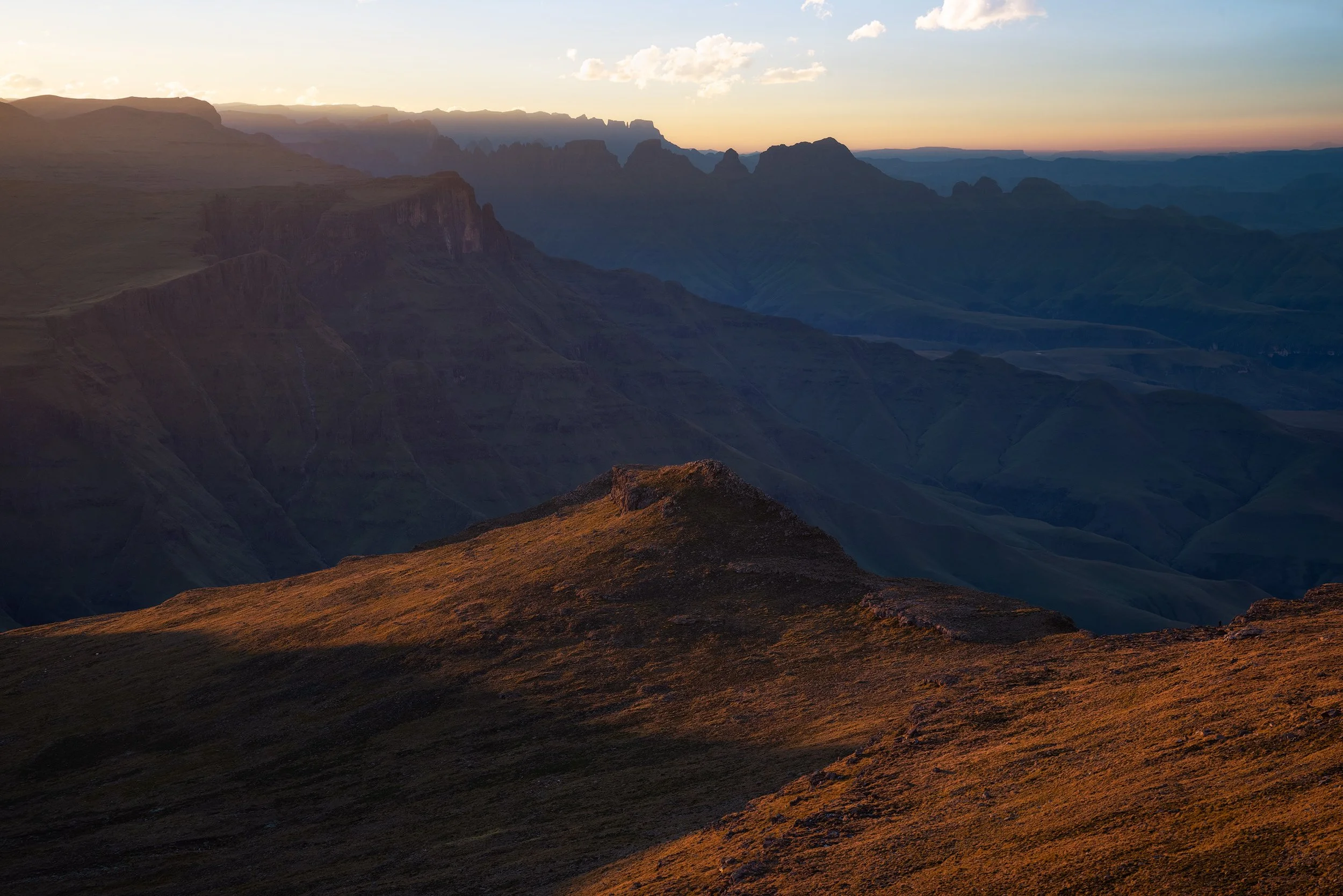 Sunset over the Grand Canyon showing layered cliffs, mesas, and ridges with a sky transitioning from orange to blue. Drakensberg, South Africa, Kwazulu Natal.