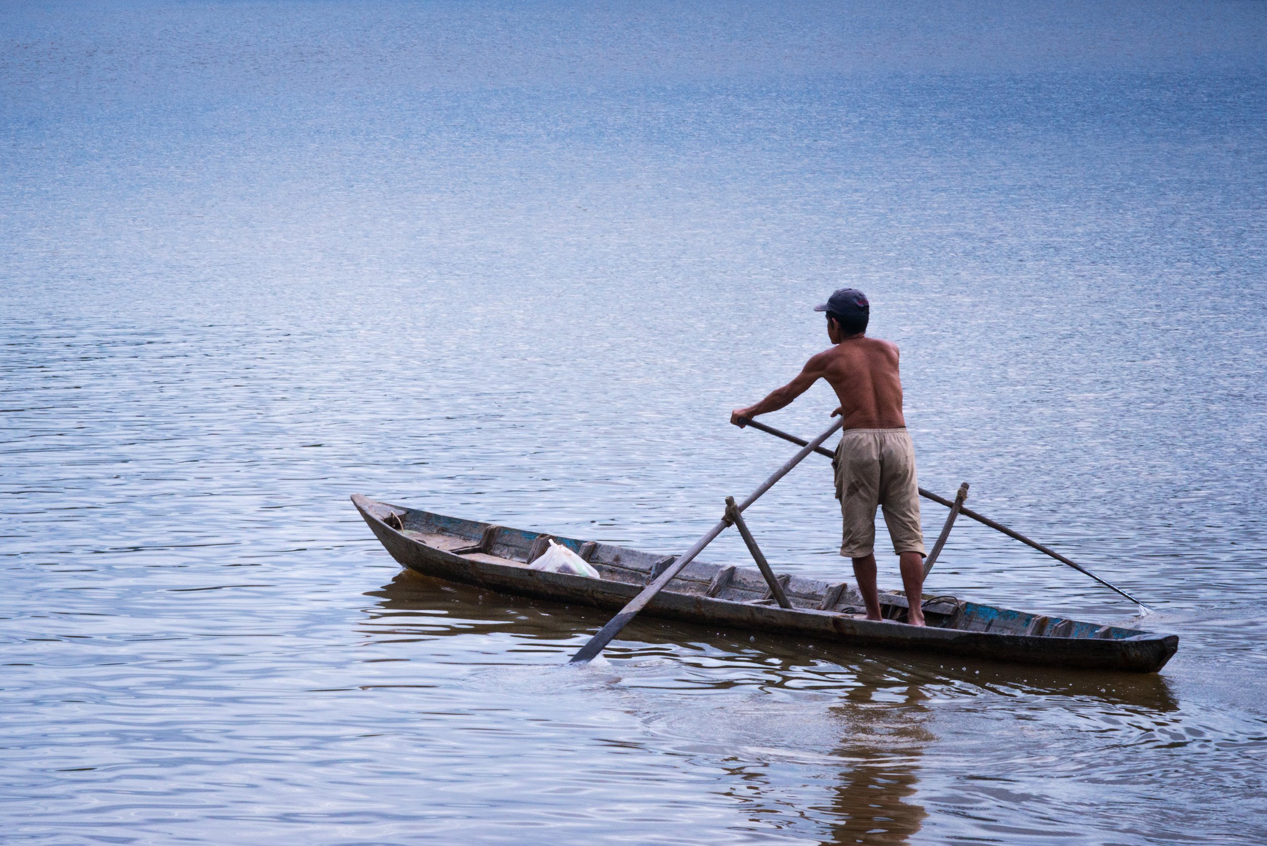 A man rowing a small boat on a lake. Cambodia.
