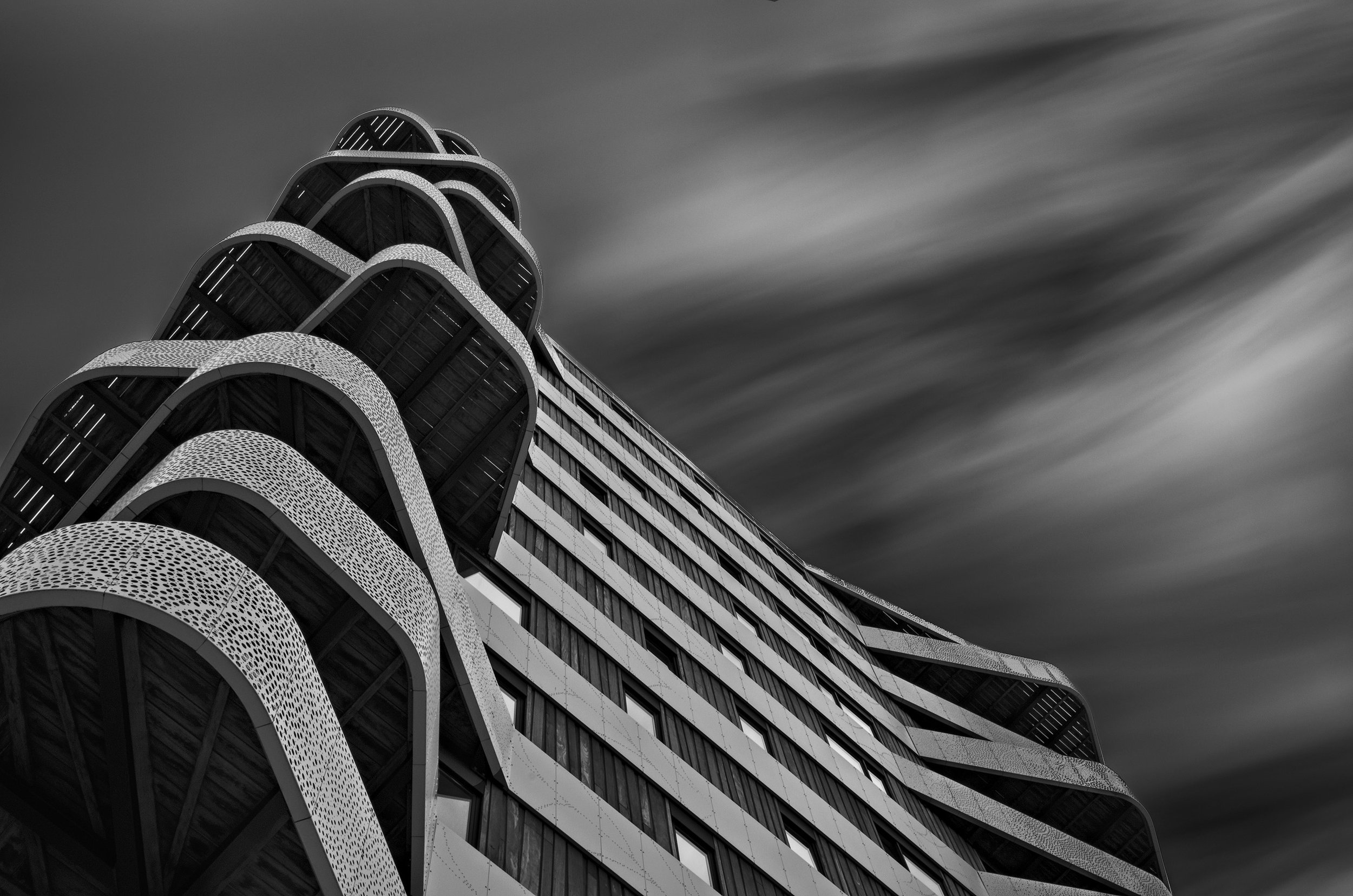 Black and white photo of a modern high-rise building with curved architecture and large windows, with a cloudy sky in the background.
