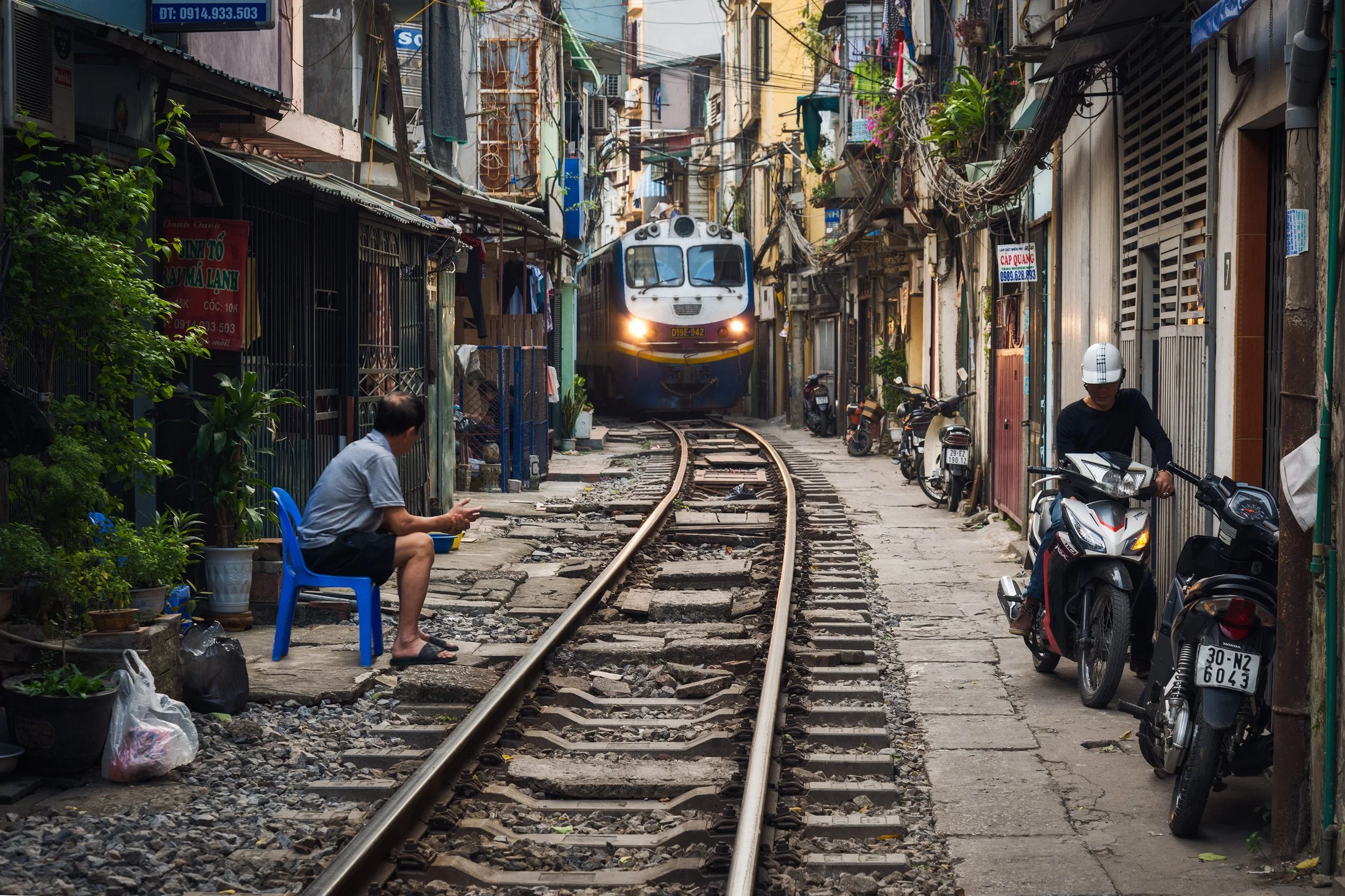 A train coming toward a narrow residential street with people and motorcycles on the sidewalk. Hanoi, Viet Nam, Vietnam
