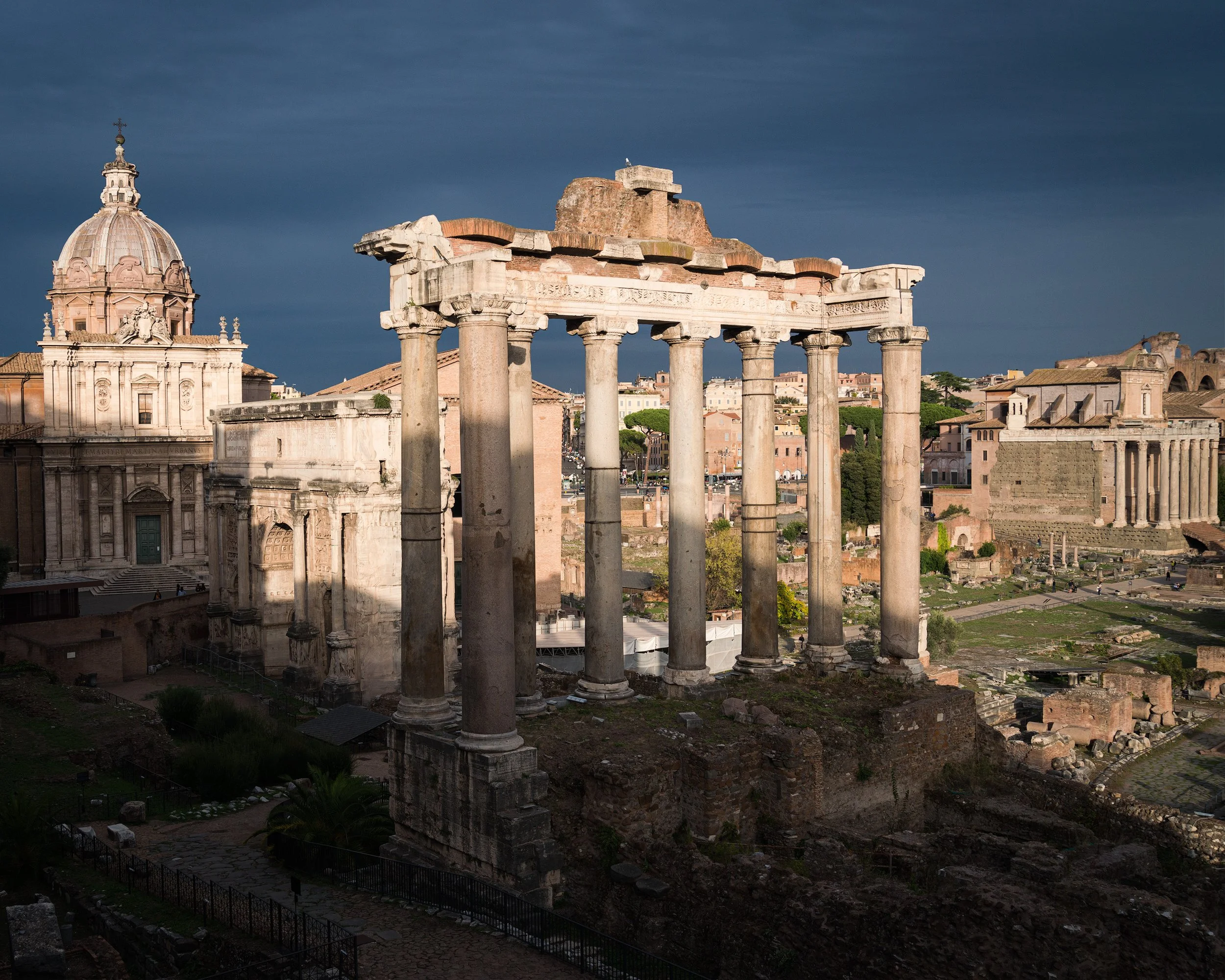 Ancient ruins of a Roman temple with tall columns, in a cityscape with historic buildings and a dark cloudy sky in Rome, Italy.