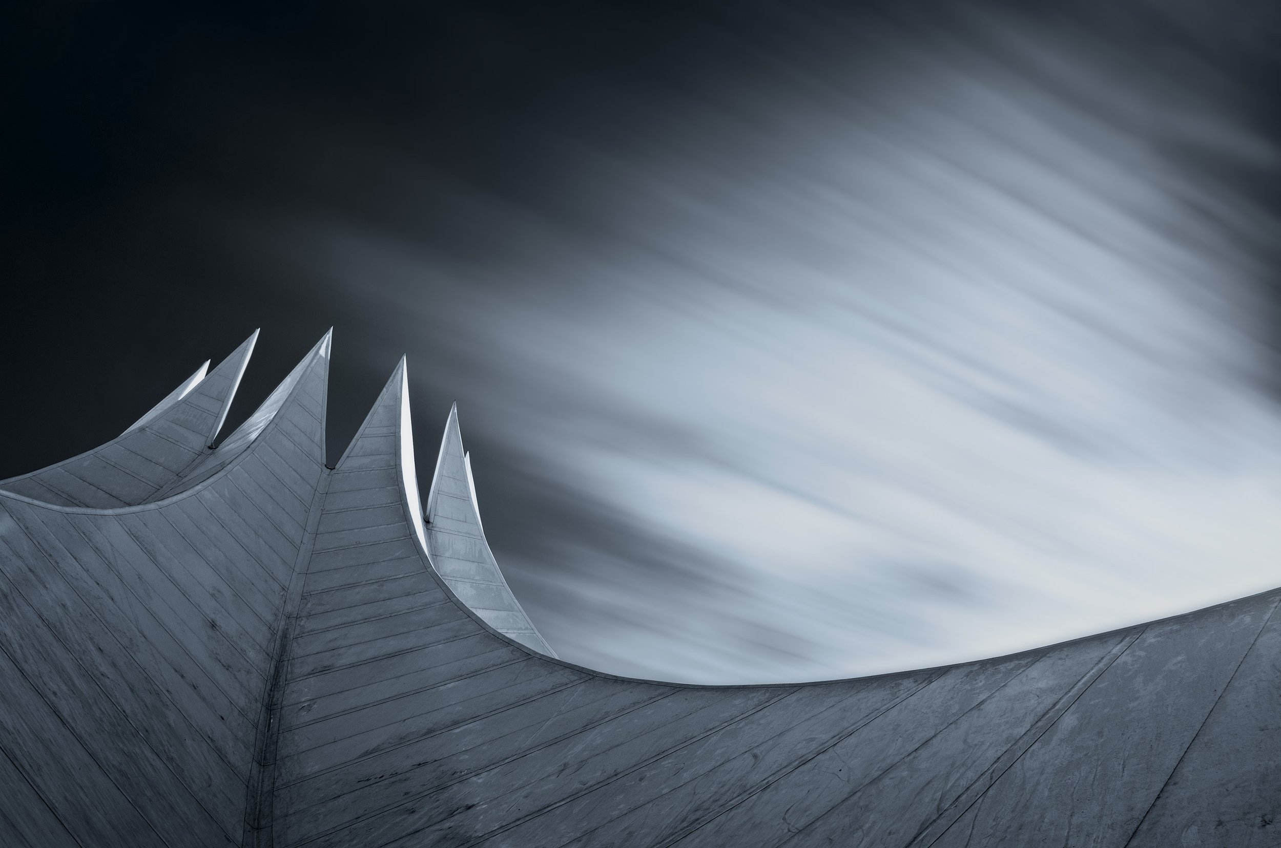 Modern architectural building with sharp, pointed peaks against a blurred sky.