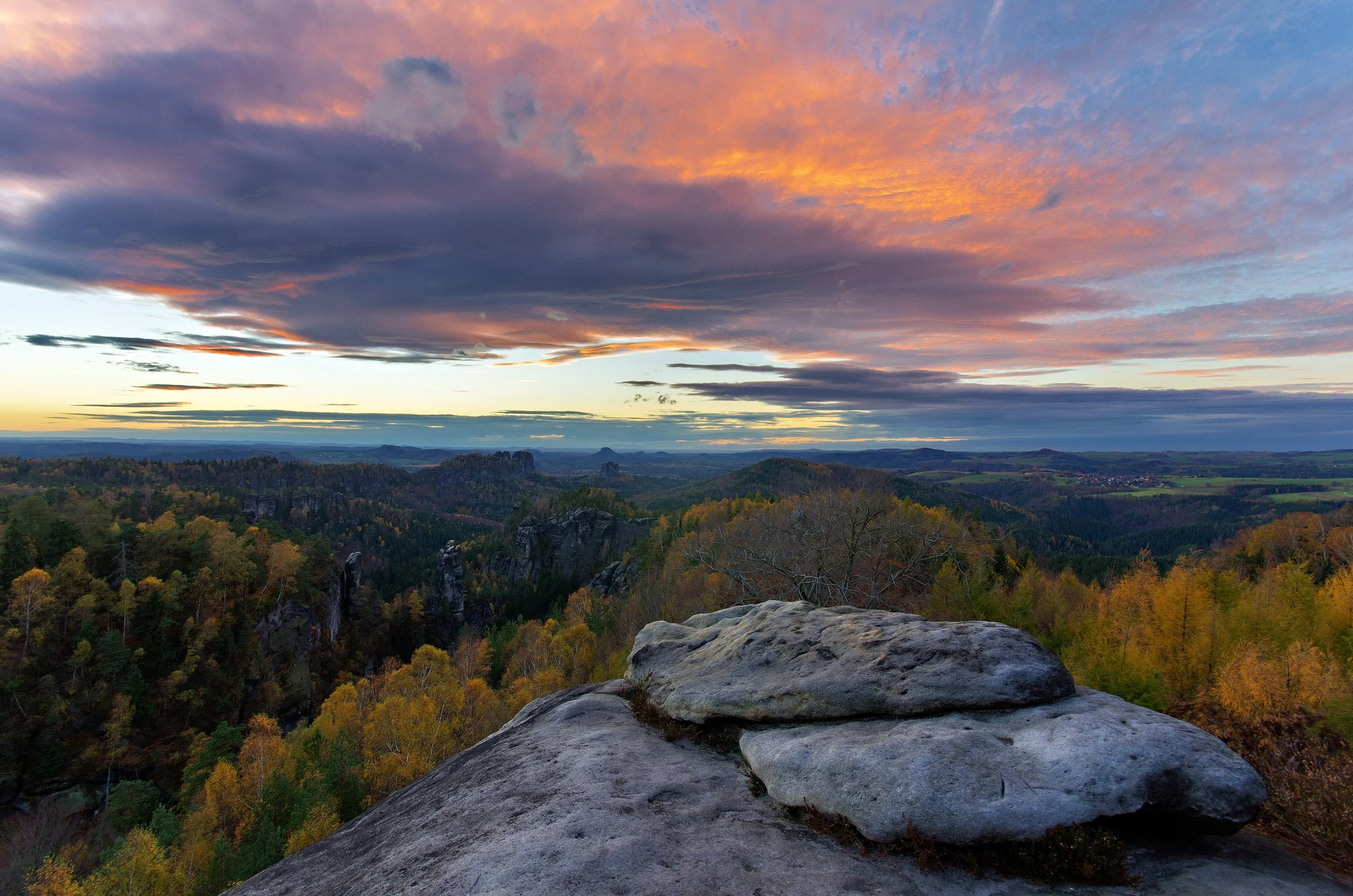 Scenic view of a sunset over a valley with rock formations and a forest, with pink and purple clouds in the sky.