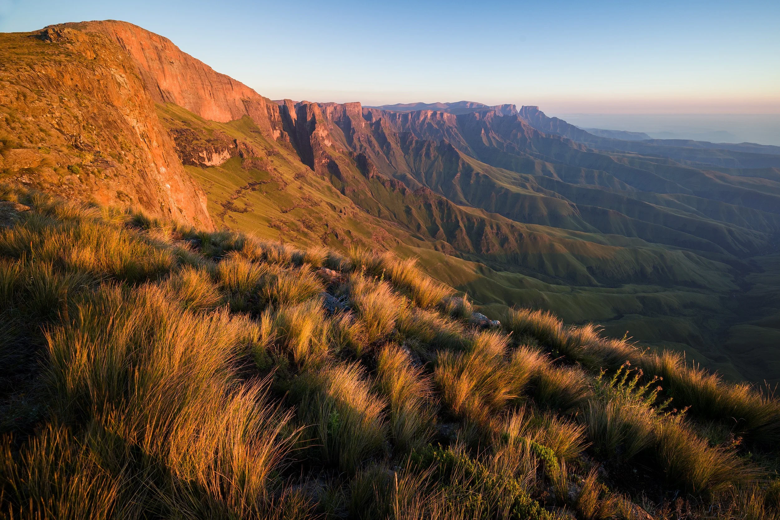 Sunset over a green mountain range with grassy slopes in the foreground Drakensberg, South Africa, Kwazulu Natal.