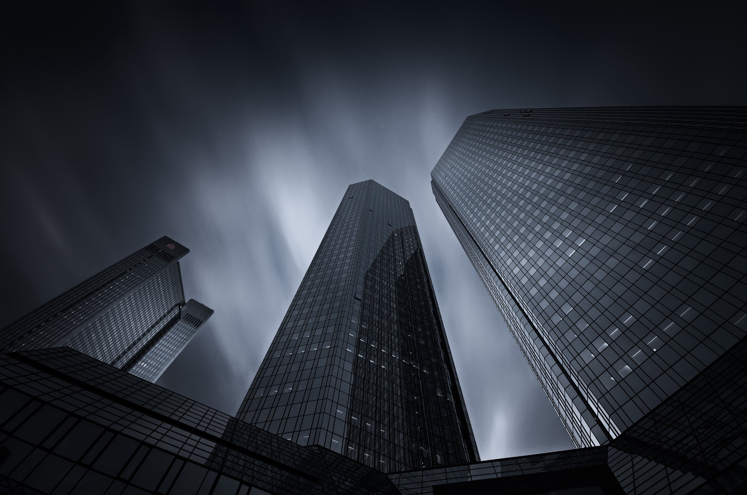 Looking up at modern glass skyscrapers against a cloudy, stormy sky.