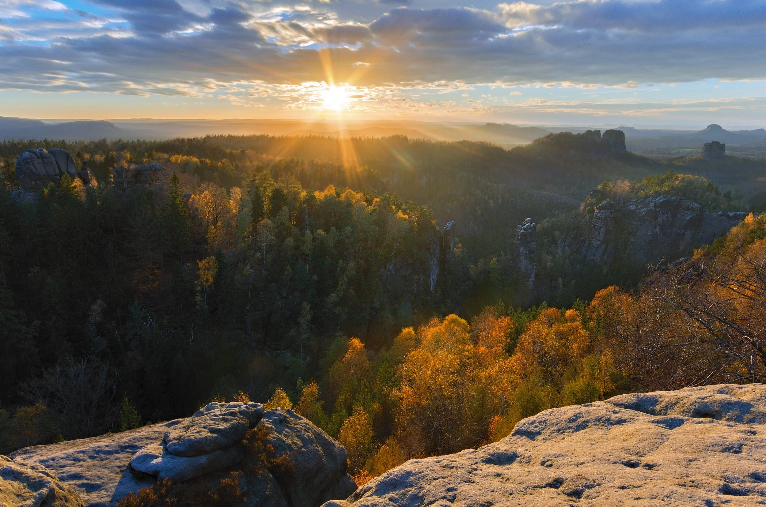 Sunset over a forested canyon with rock formations and colorful autumn trees.