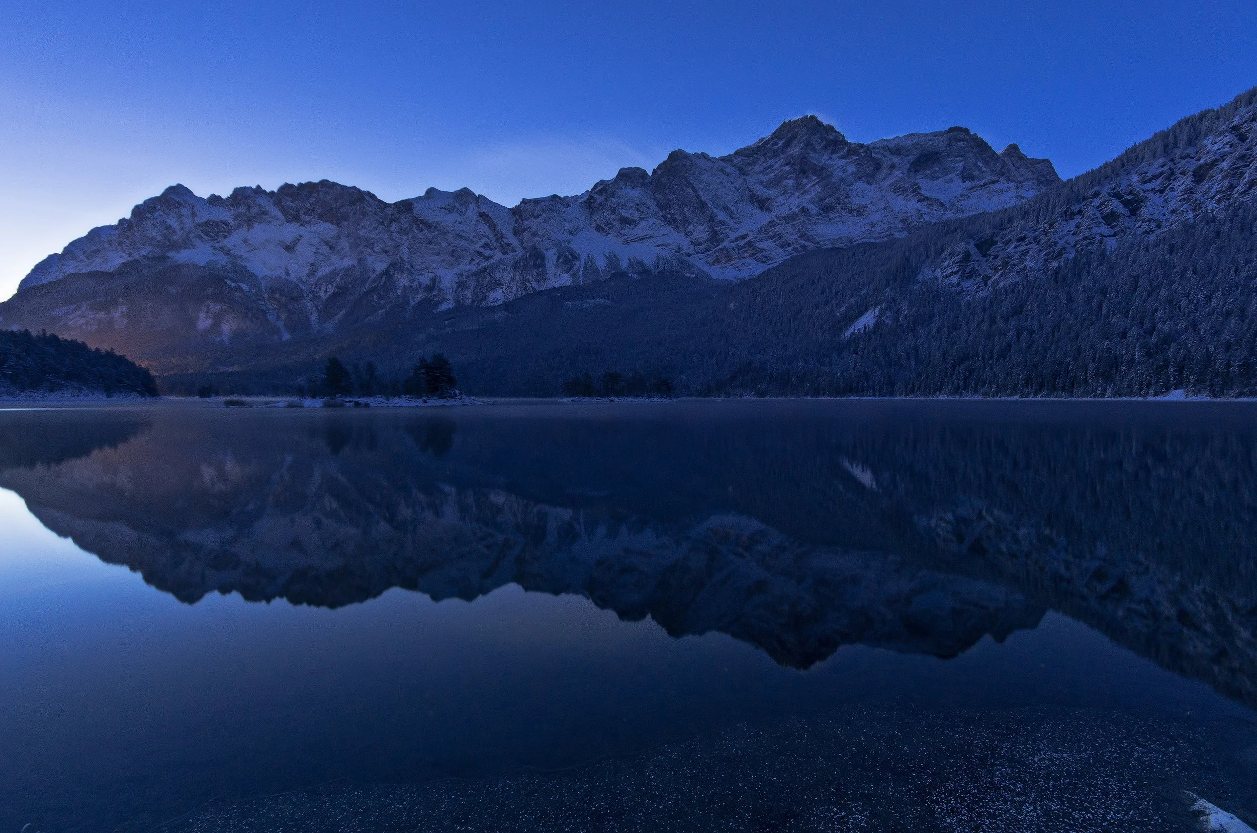 Snow-capped mountains reflected on a still lake at dusk.