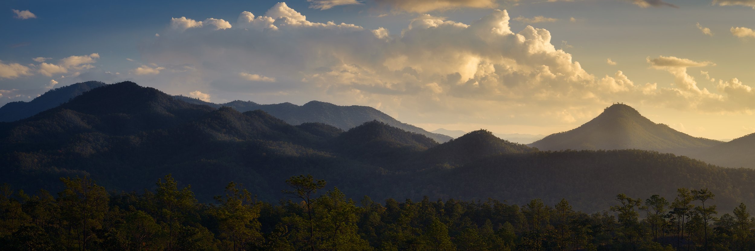 Mountain range during sunset with clouds in the sky and a forest in the foreground. Pai, Thailand.