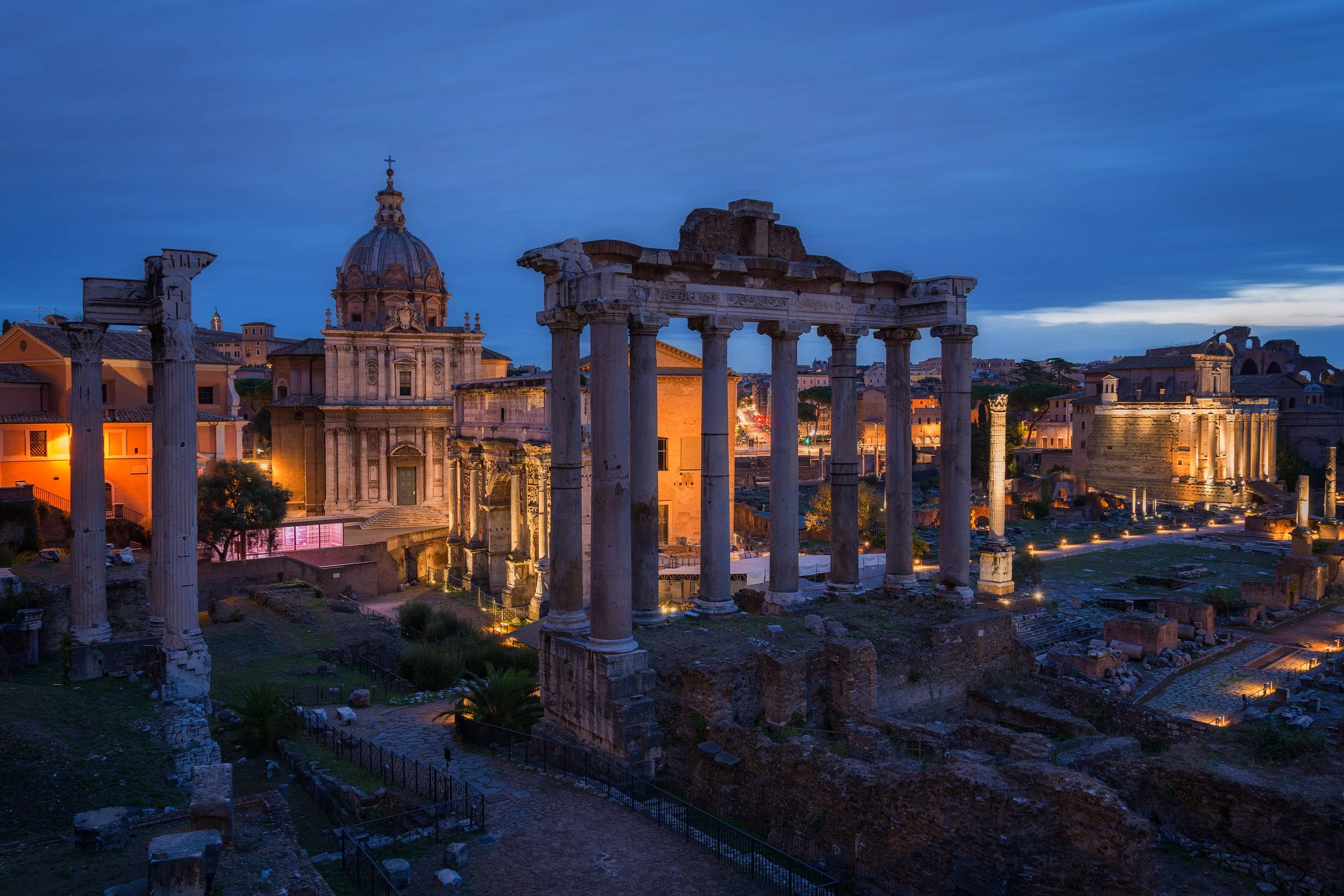 Ancient ruins of Roman columns and structures illuminated at twilight in a historic city.