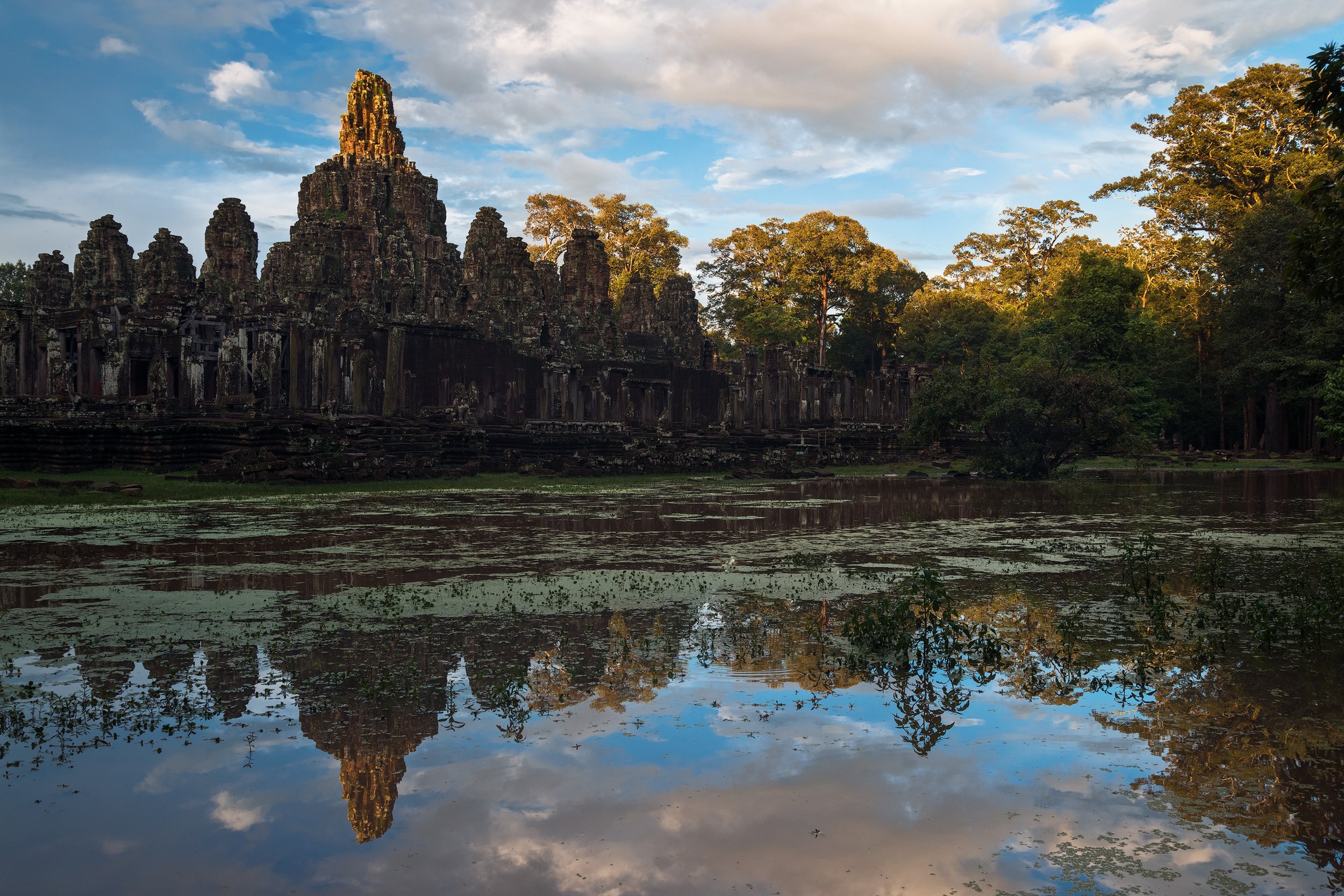Sunset over ancient stone temple with reflections in water, surrounded by trees. Angkor Wat Cambodia.
