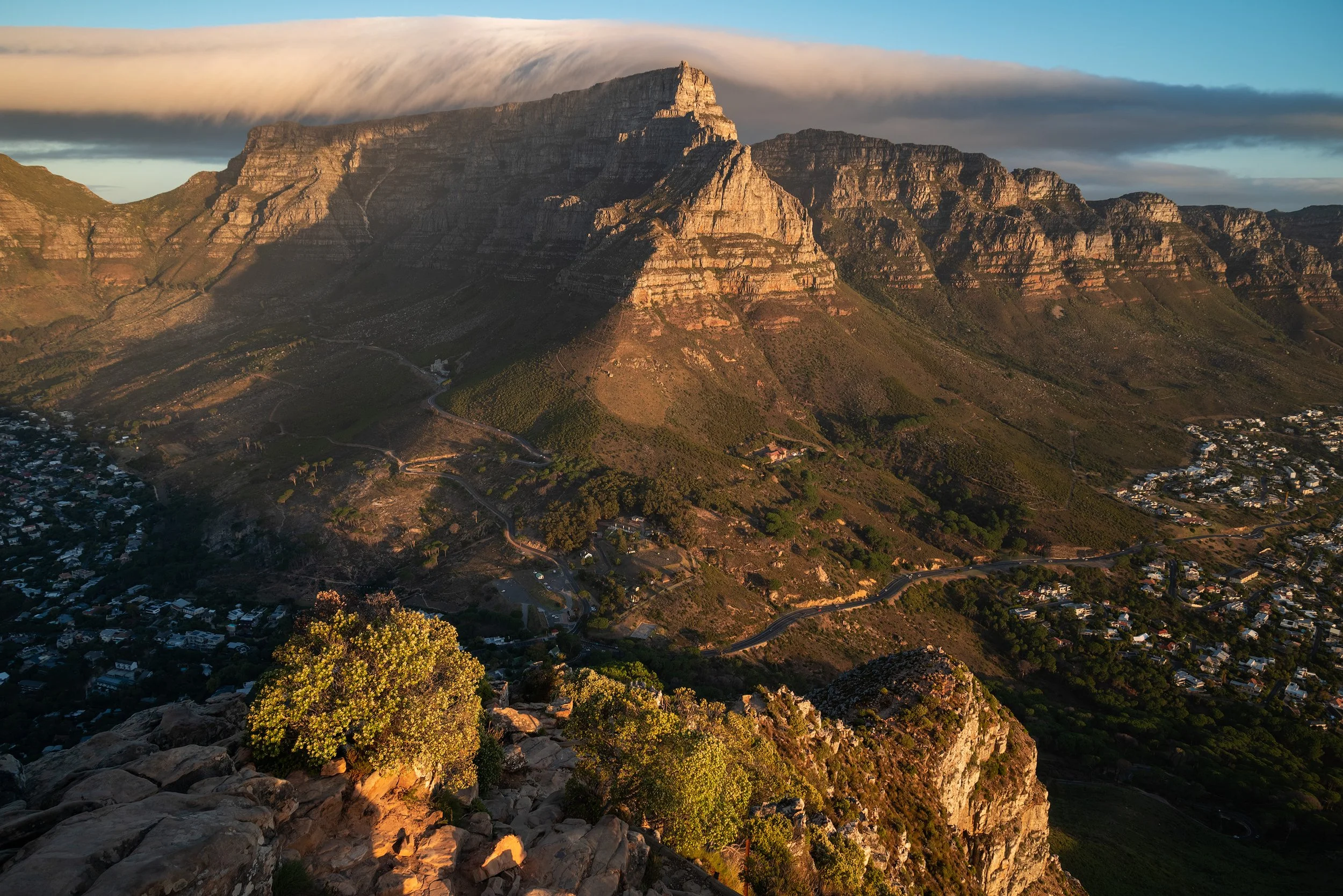 A view of Table Mountain in South Africa during sunset with cloud formation above it, overlooking the surrounding city and landscape. Cape Town