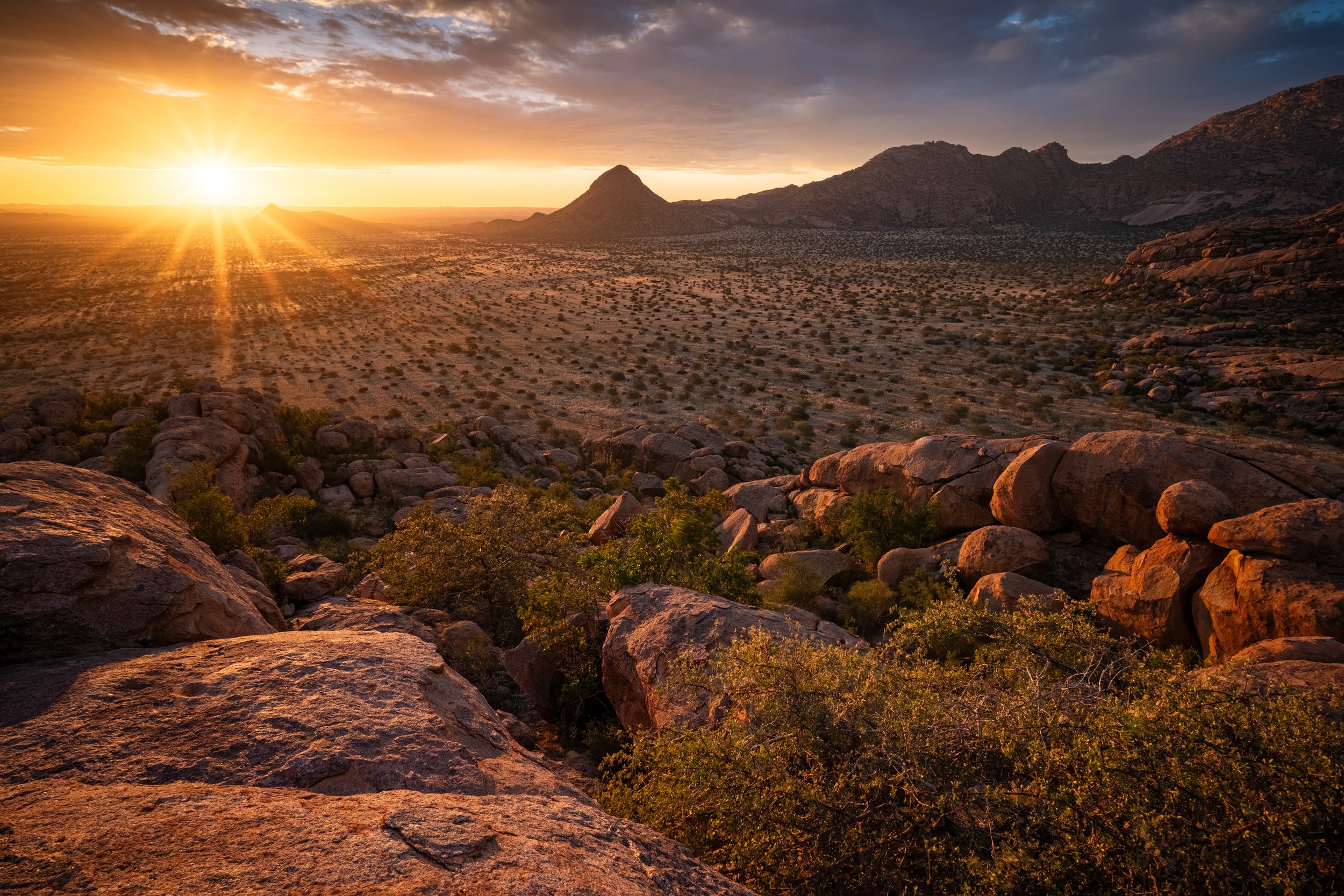 Sunset over Erongo mountains in Namibia. a desert landscape with rocky terrain, sparse vegetation, distant mountains, and a partly cloudy sky.