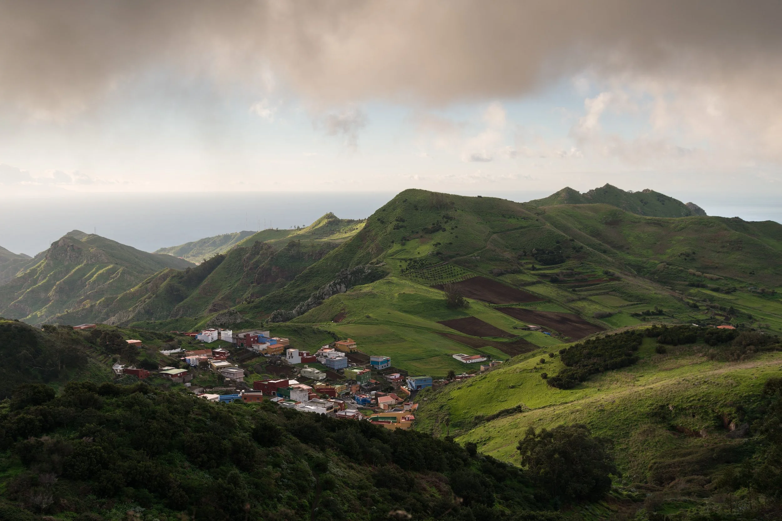 Green mountains with a small village at the base, under a cloudy sky. Tenerife