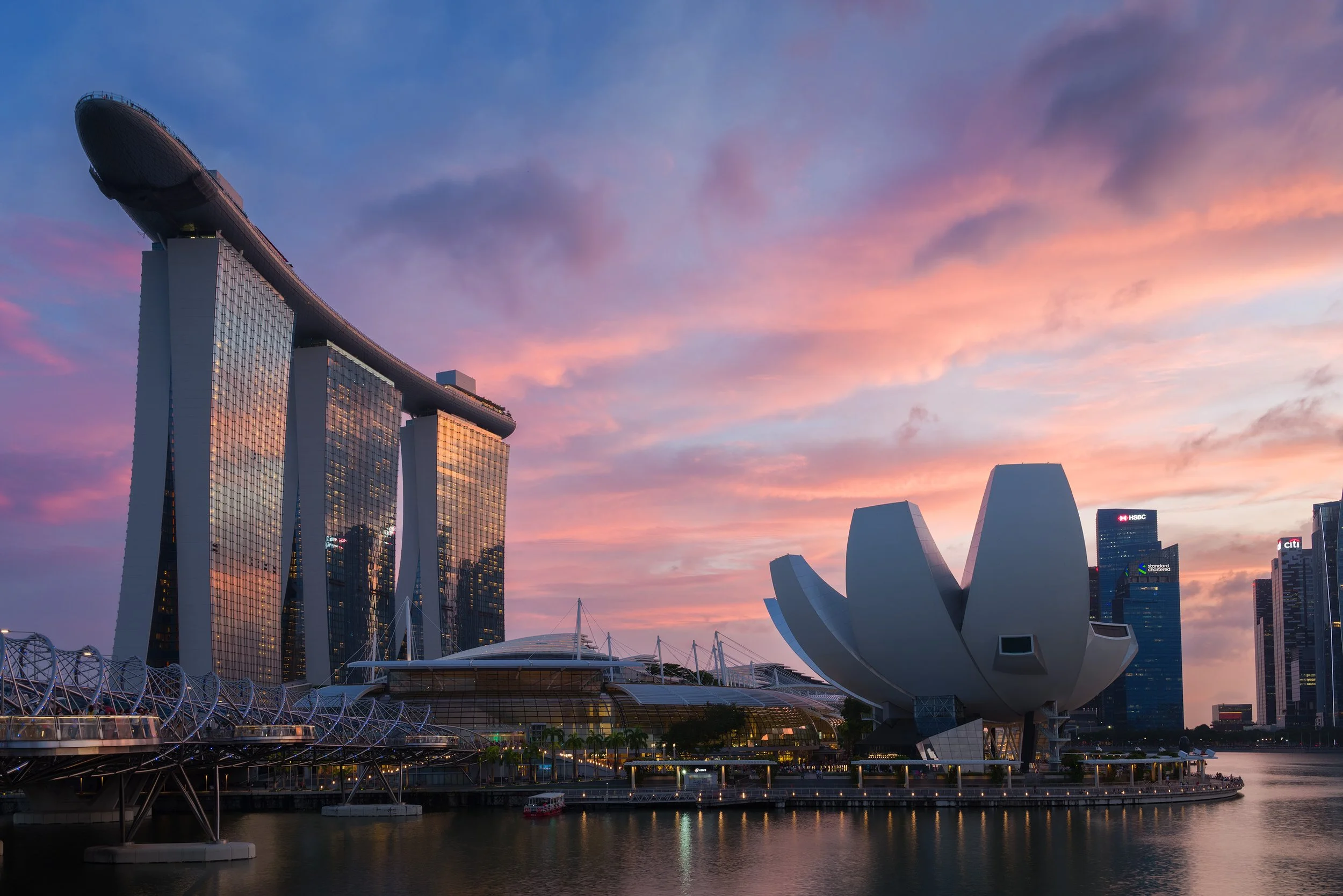 Singapore skyline at sunset featuring Marina Bay Sands hotel with its boat-shaped top, ArtScience Museum shaped like a lotus flower, and surrounding skyscrapers.