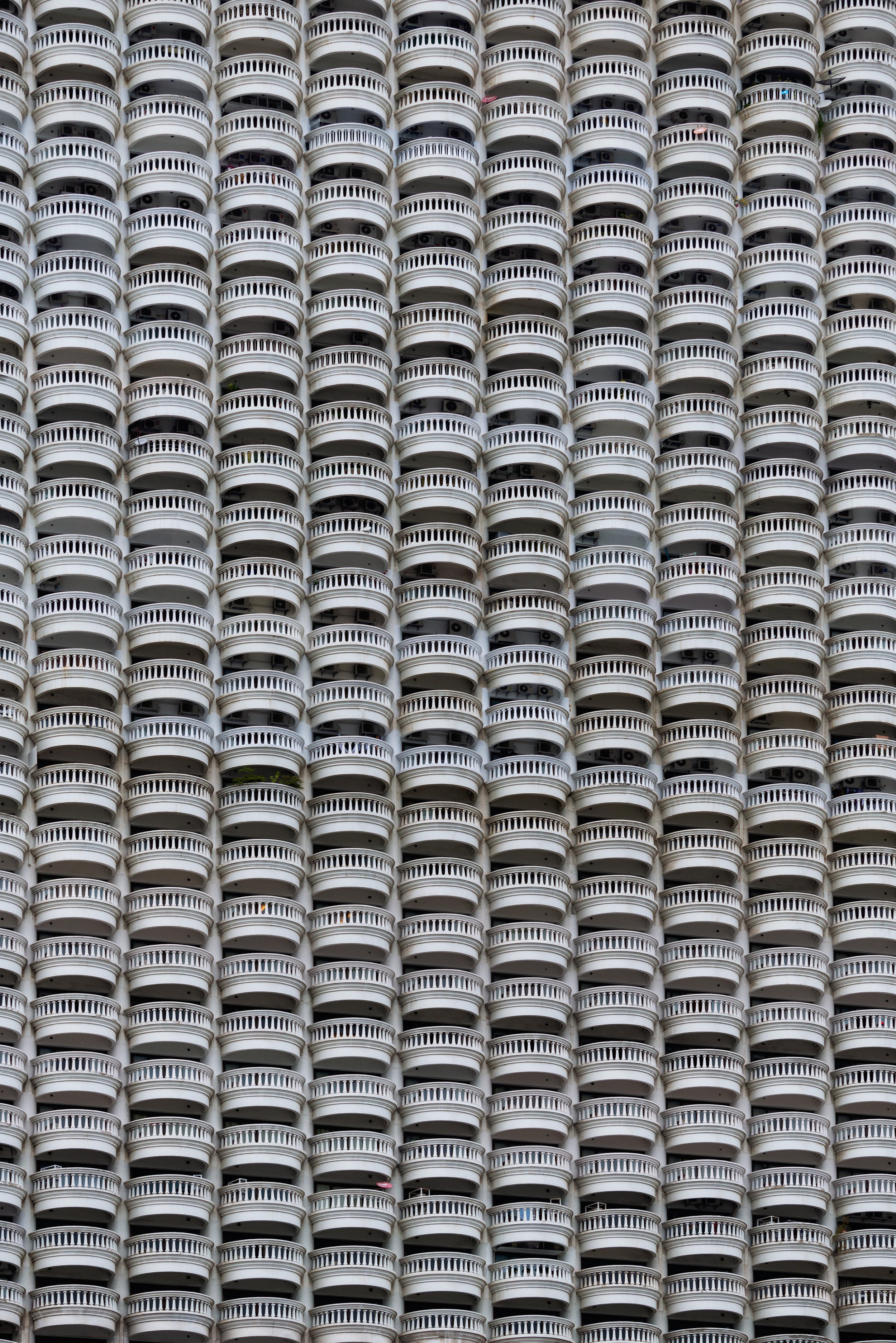 A building in Bangkok with numerous white, rounded balconies with railings, creating a repetitive pattern across the facade.