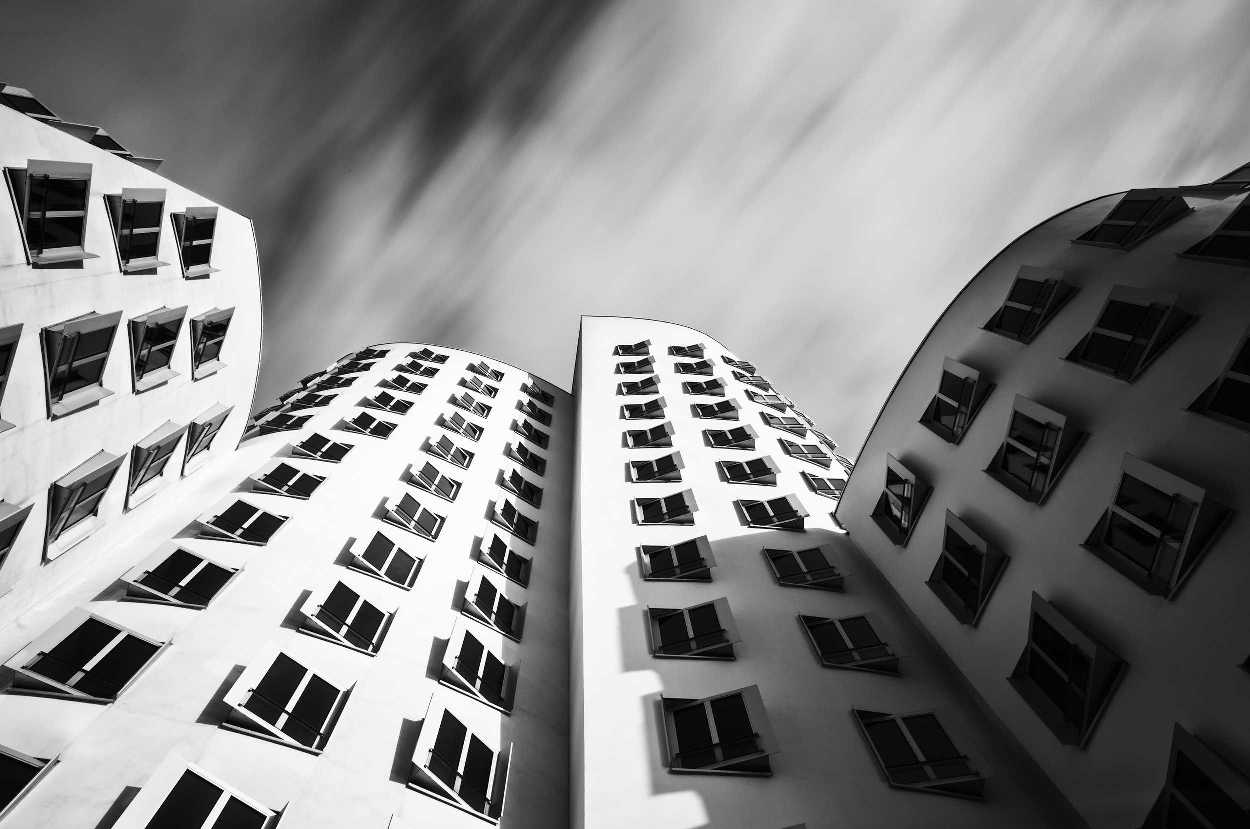 Black and white photo of three modern buildings with curved facades and many windows, taken from a low angle looking up at the sky.