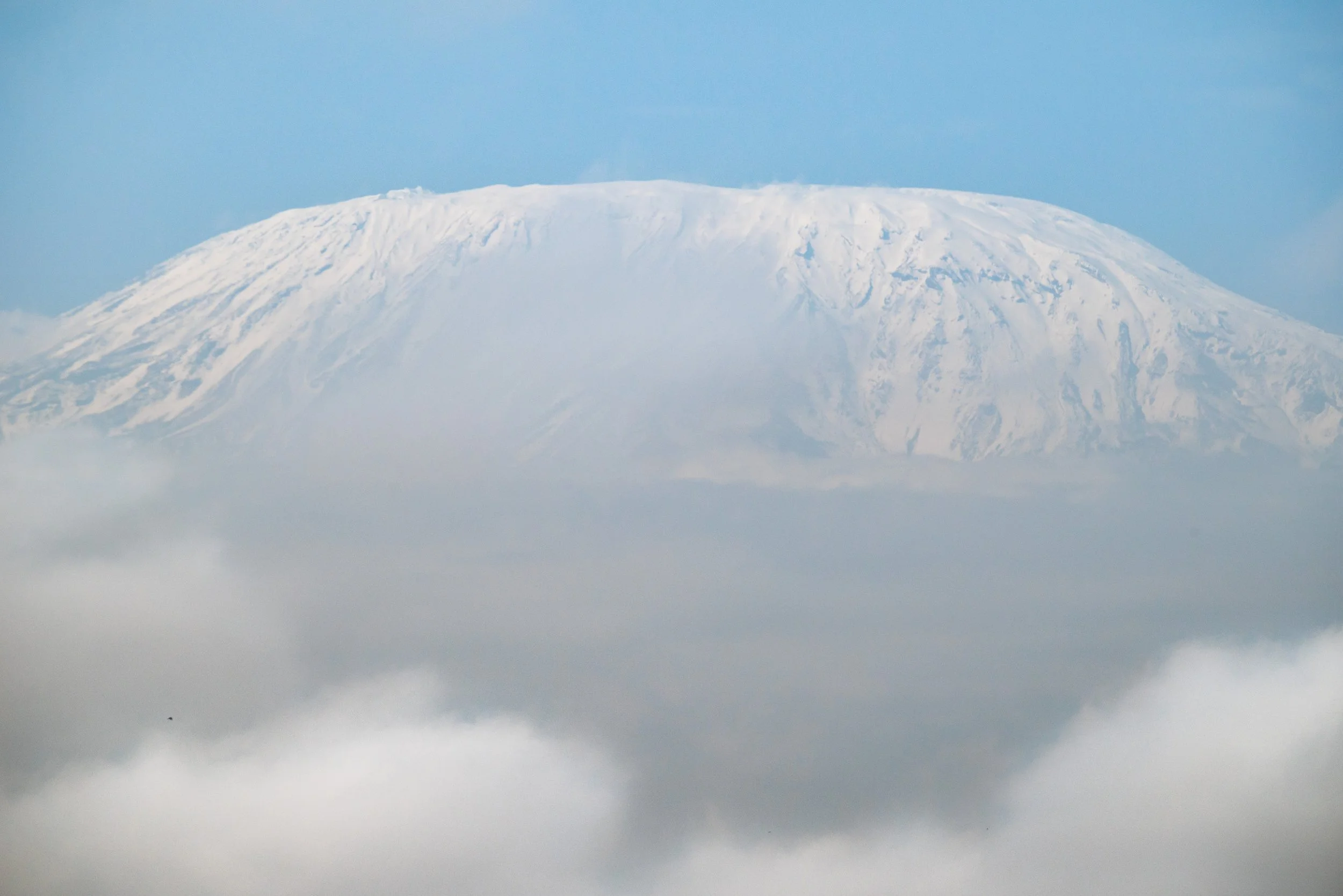 Snow-capped mountain peak above a layer of clouds in the sky.