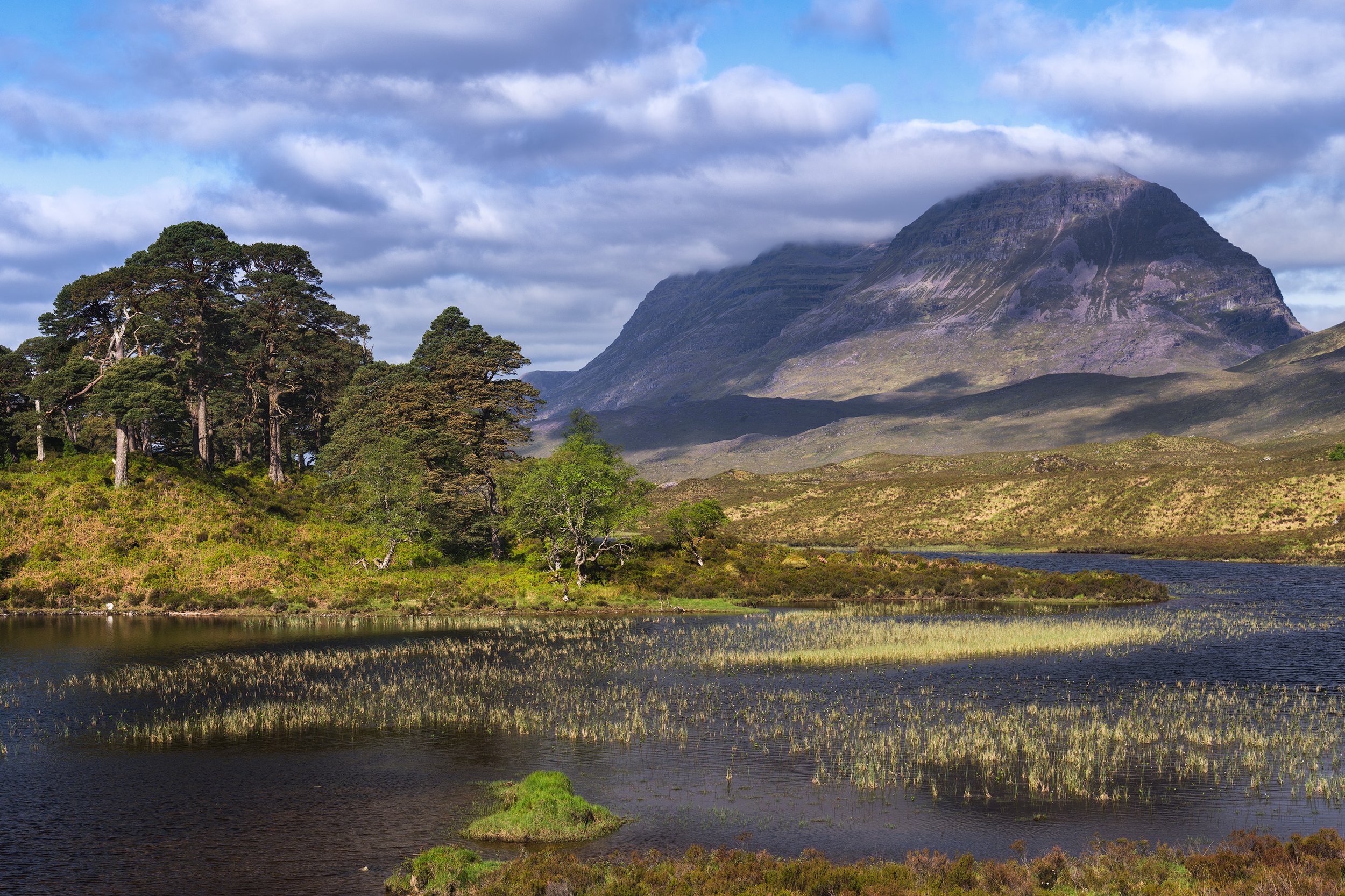 Scenic Scottish landscape of a mountain range with a lake and green trees in the foreground.