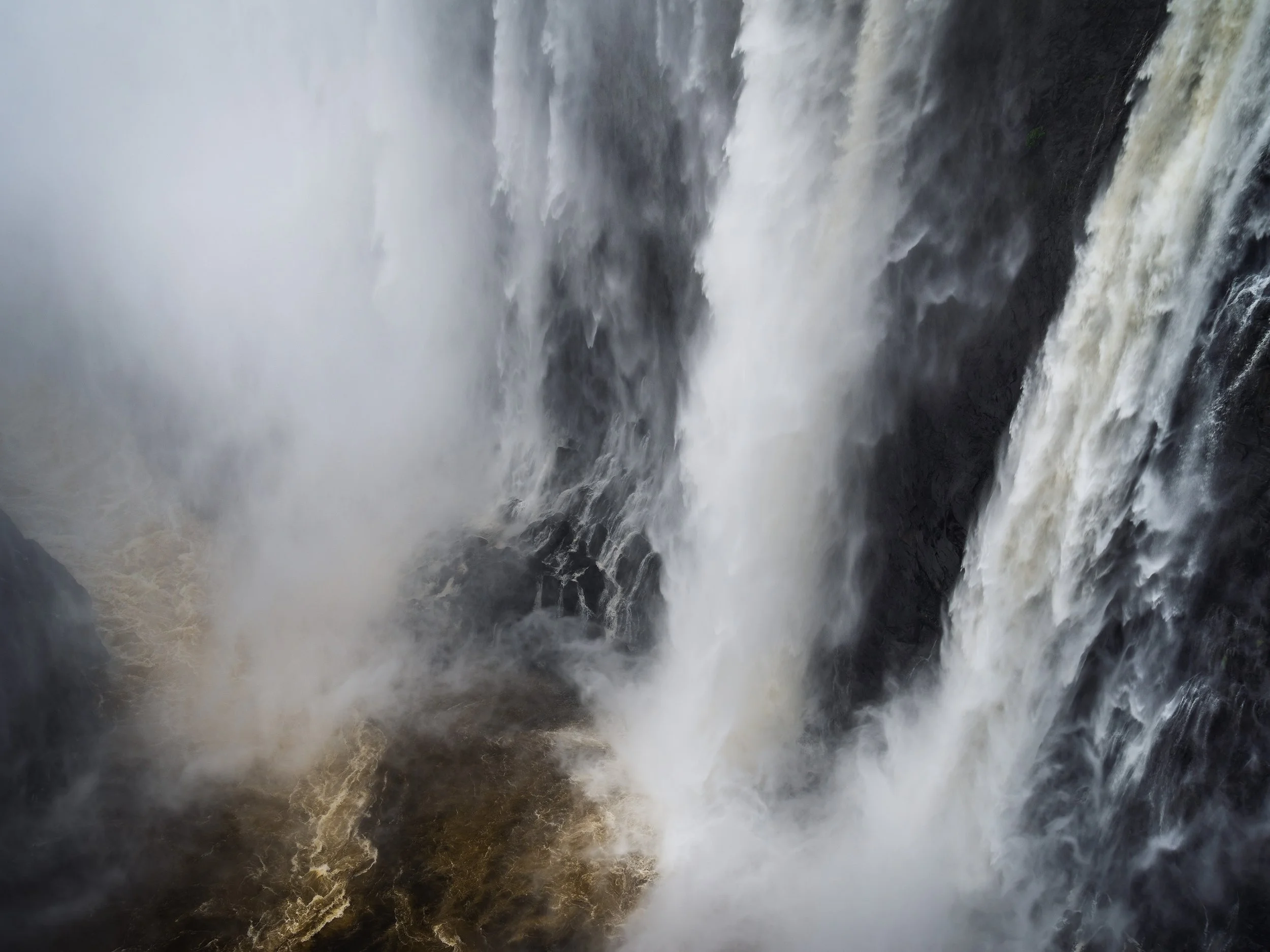 A powerful waterfall crashing down into a river below, surrounded by dark rocks and mist.