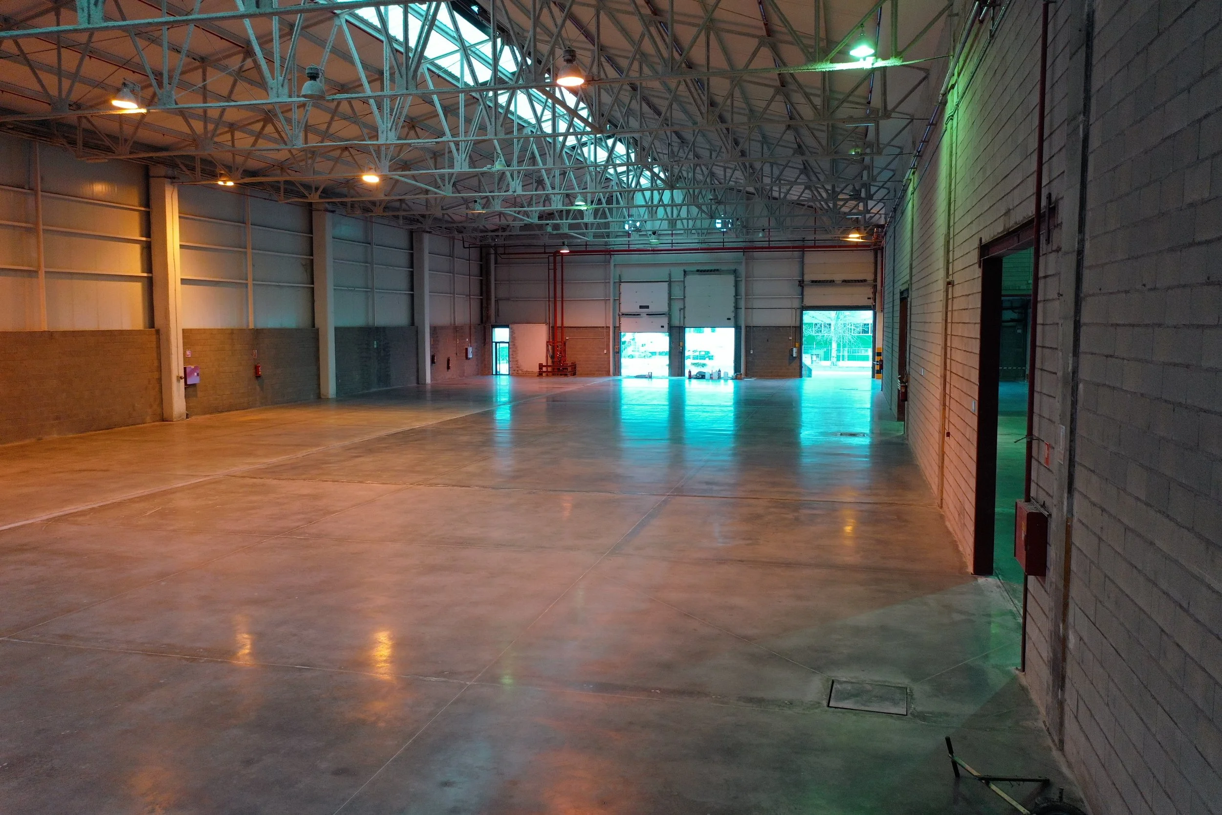 Empty industrial warehouse with large open floor, high ceiling with metal beams, and a large open garage door letting in natural light treated with the RINOL DRT system.