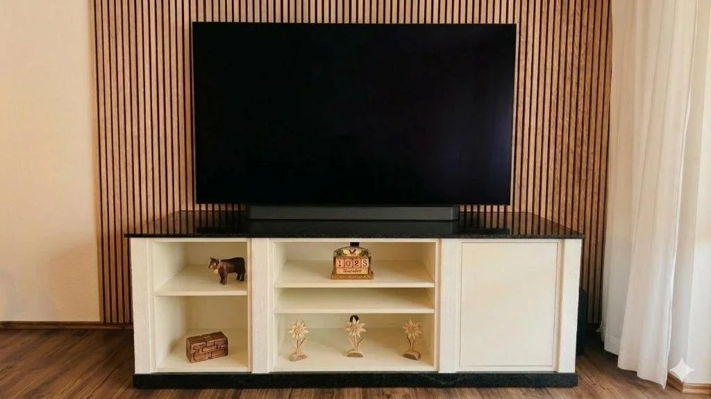 Berg Fux Ferienhaus Grüntenblick Ein Fernseher steht auf einem weißen TV-Möbel mit offenen Fächern, das vor einer Wand mit vertikal angebrachten Holzpaneelen steht.