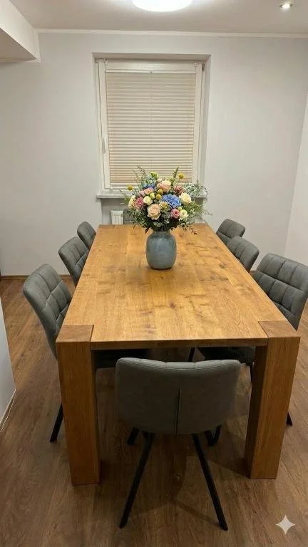 Berg Fux Ferienhaus Grüntenblick Ein Esstisch mit acht gepolsterten Stühlen in einem hellen Raum. In der Mitte des Tisches steht eine große Vase mit buntem Blumenstrauß.