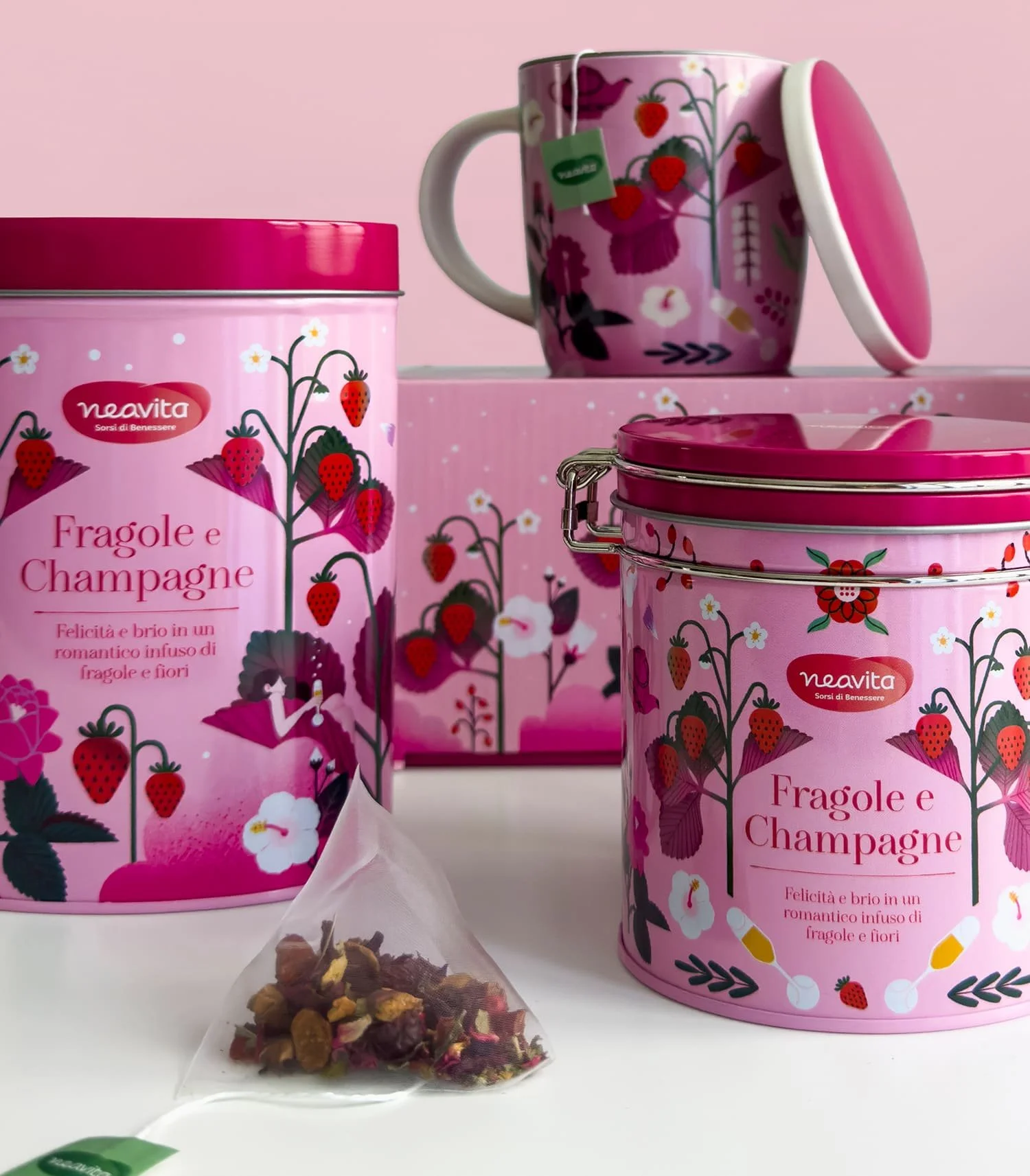 Confezioni di tè con il marchio Neavita, decorazioni a tema fragole, champagne e fiori, un sacchetto di tè con frutta essiccata davanti e una tazza con una teiera decorata con lo stesso tema