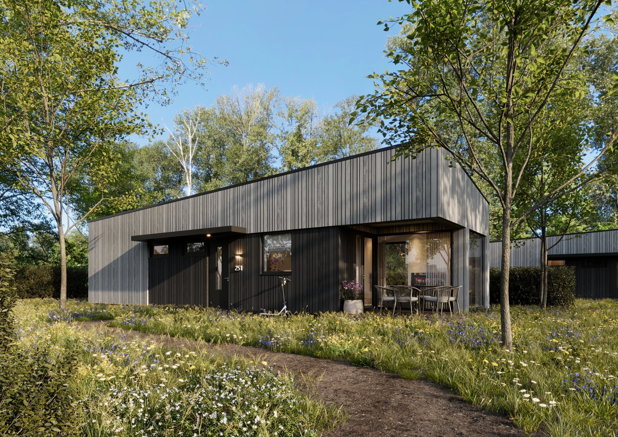 Een modern zwart houten huis met grote ramen, omringd door groene bomen en een bloementuin, onder een blauwe hemel.