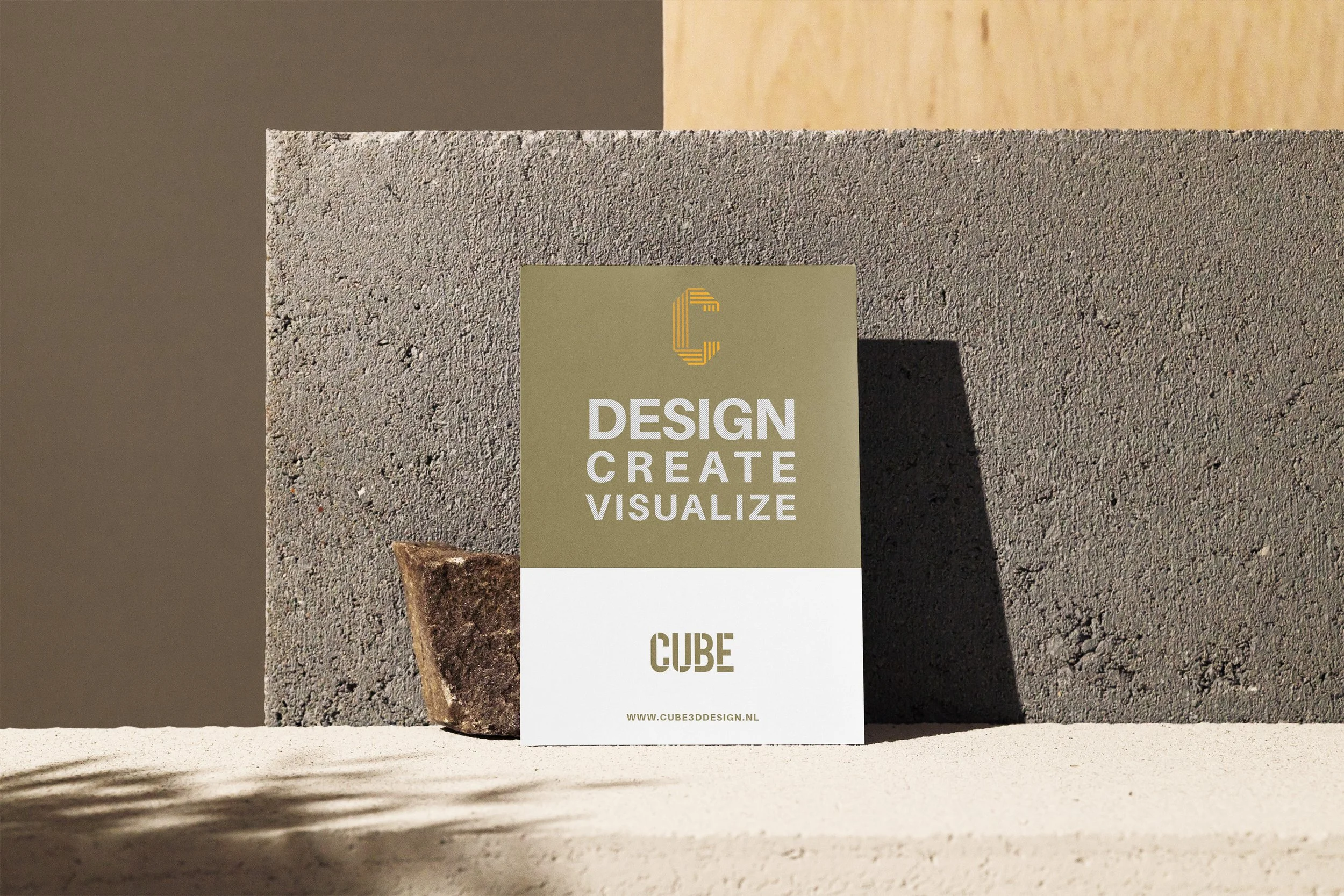 Een kartonnen poster met de tekst 'Design Create Visualize' en 'Cube', geplaatst tussen bakstenen en een cementmuur, met een schaduw die erover valt.