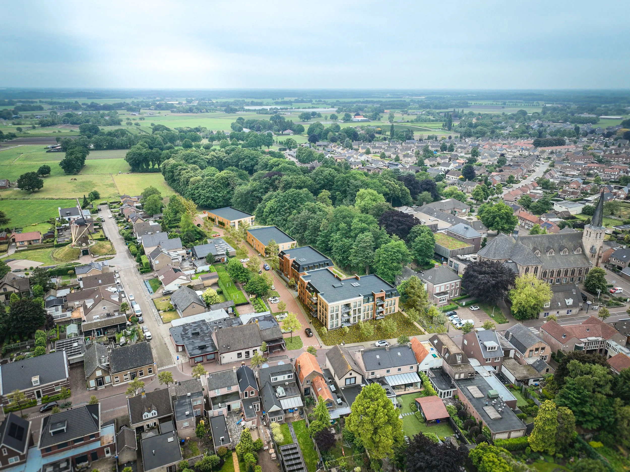 Luchtfoto van een dorp met huizen, bomen, velden en een kerk met een toren, onder een bewolkte hemel.