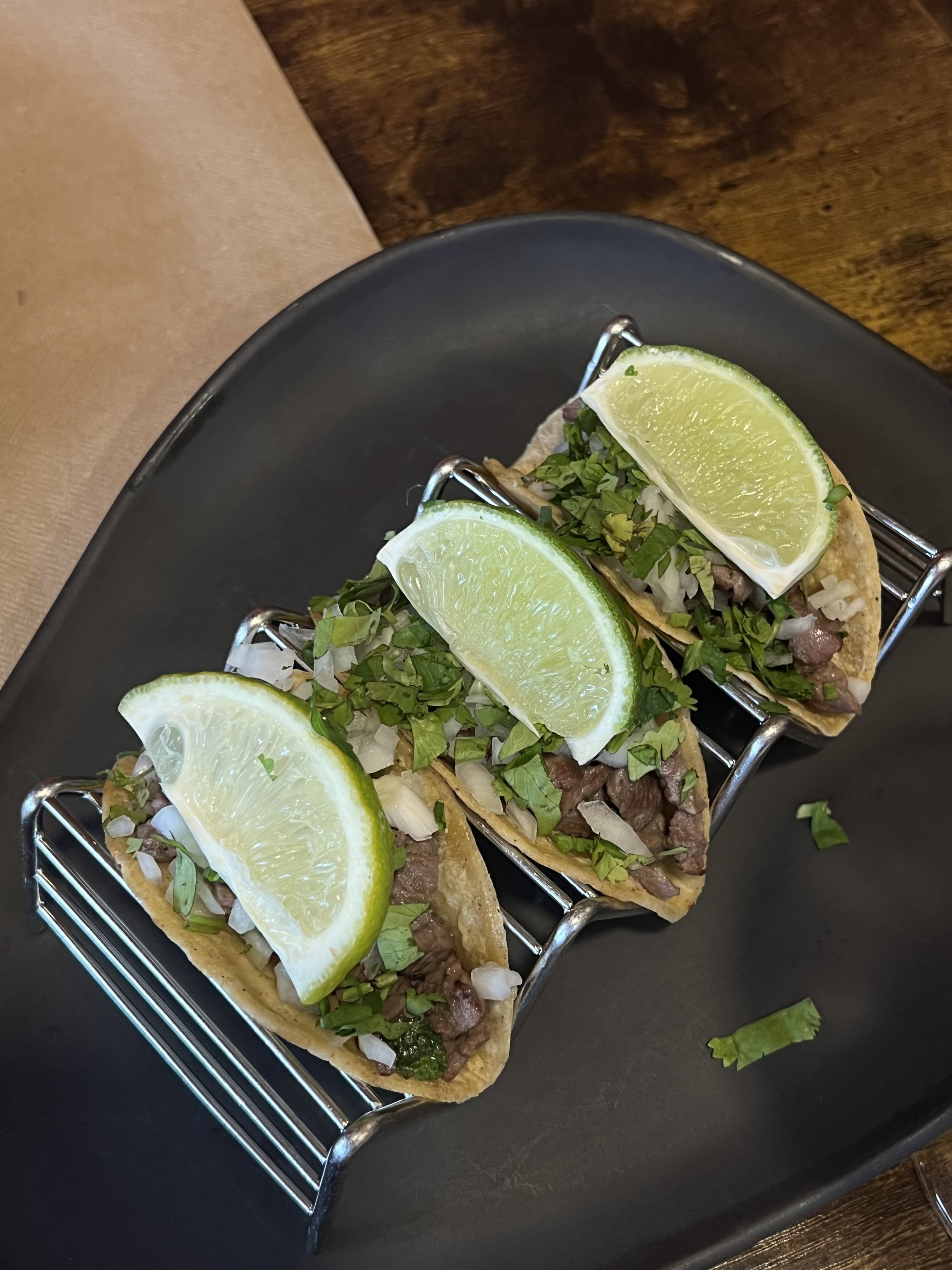 Tres tacos de ternera, cebolla y lima colocados en una bandeja sobre un plato negro