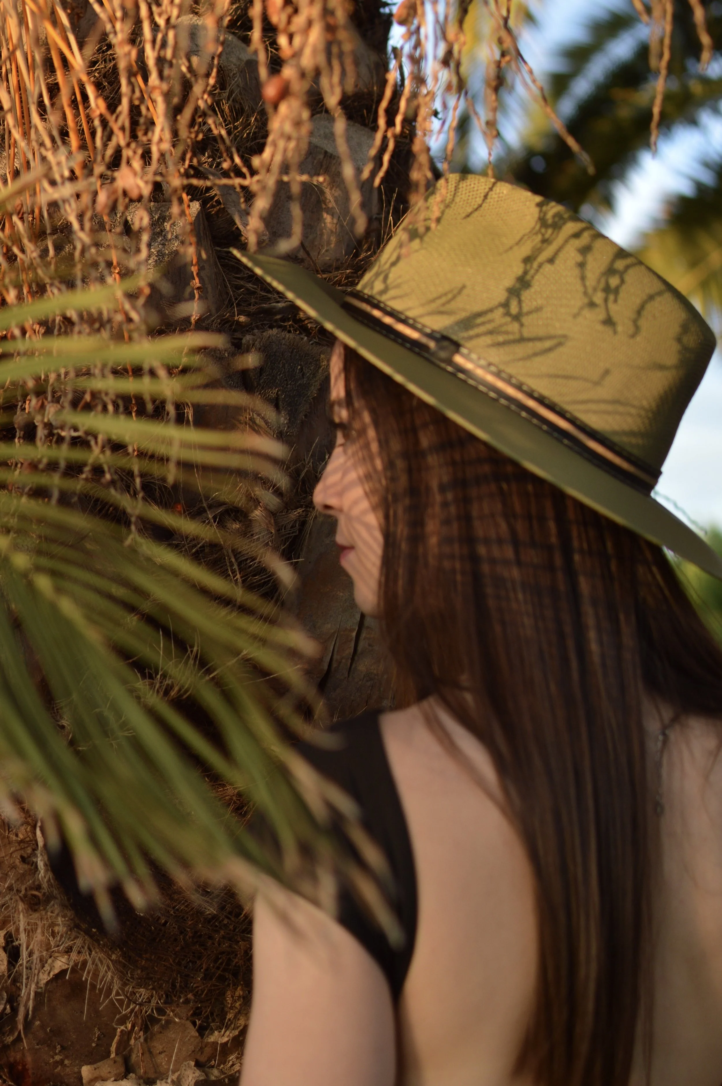 Foto de una modelo en una palmera capturada desde atrás con un vestido con la espalda al aire y un sombrero