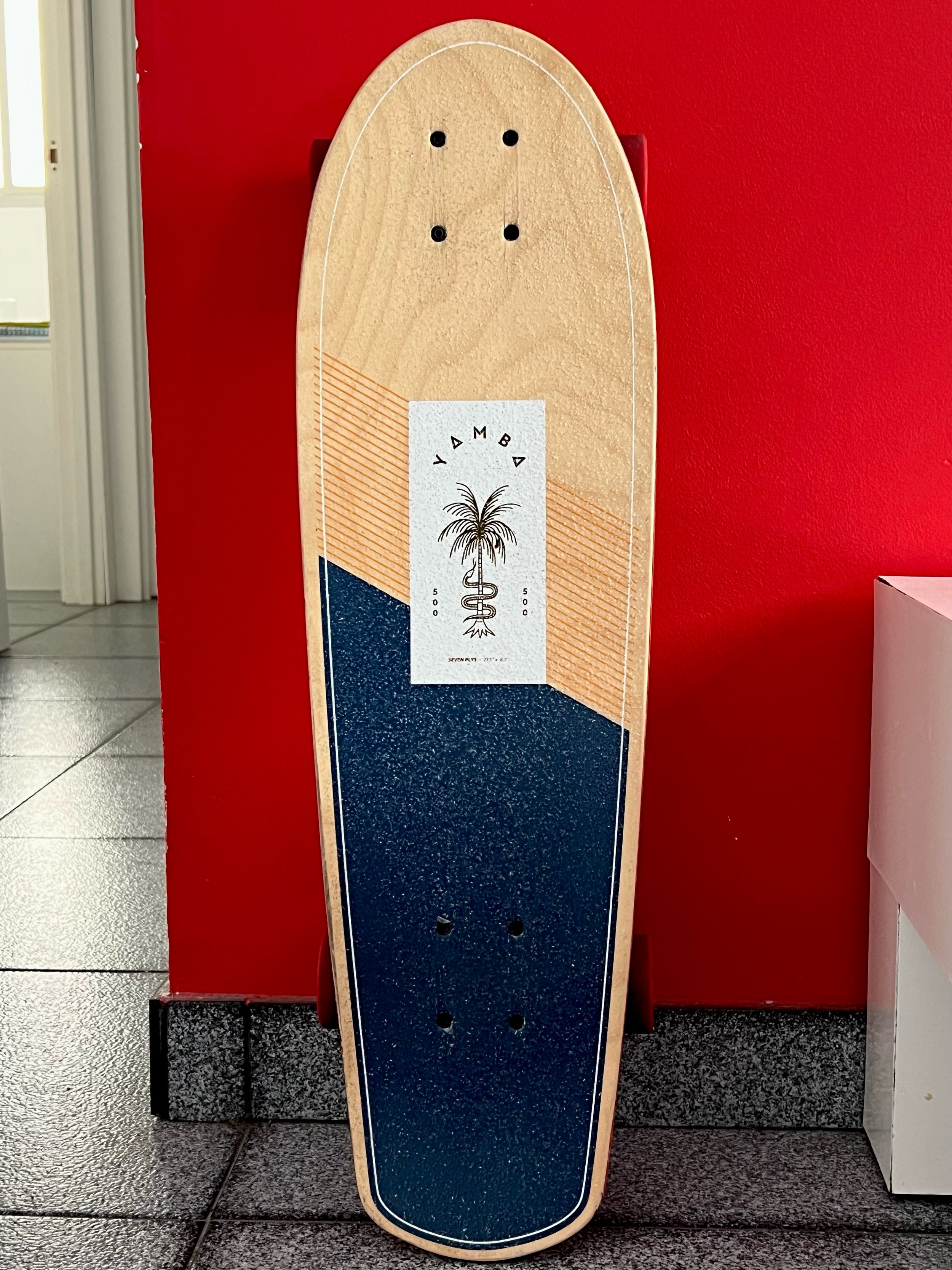 Monopatín azul y beige apoyado sobre una pared roja