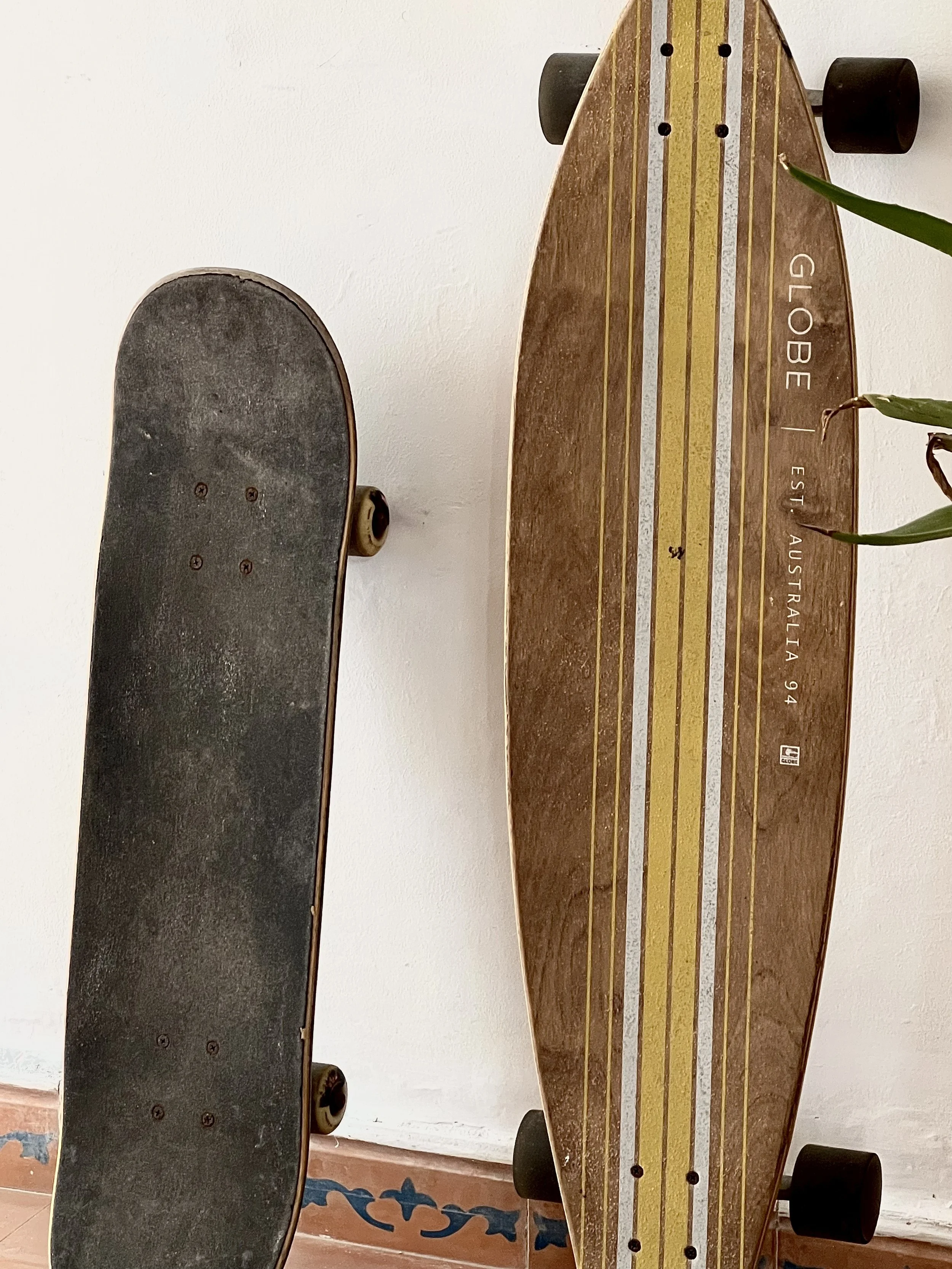 Un skate y un surfskate apoyados en una pared blanca