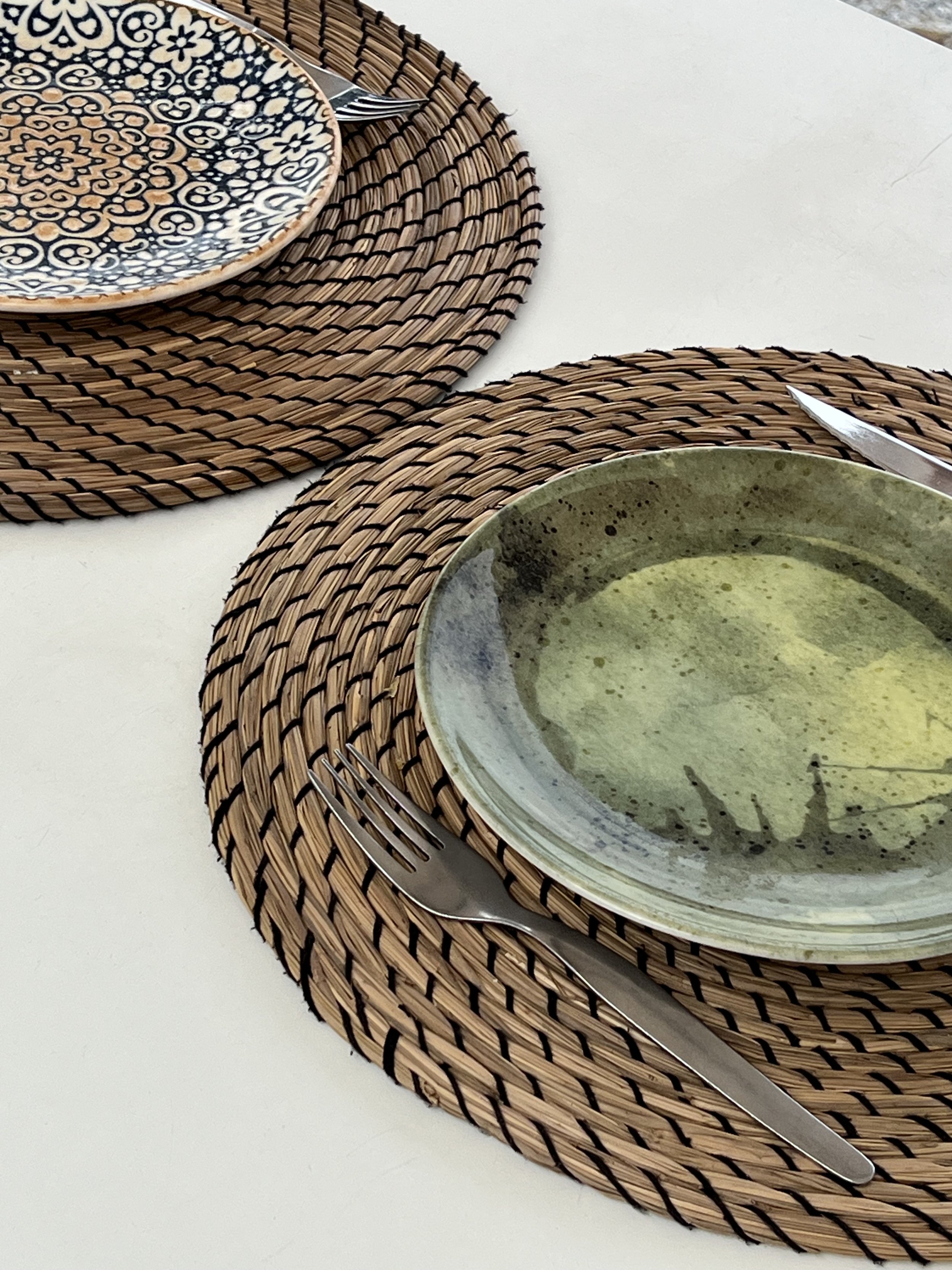 Plato verde y plato geométrico colocados en una mesa sobre un mantel de mimbre