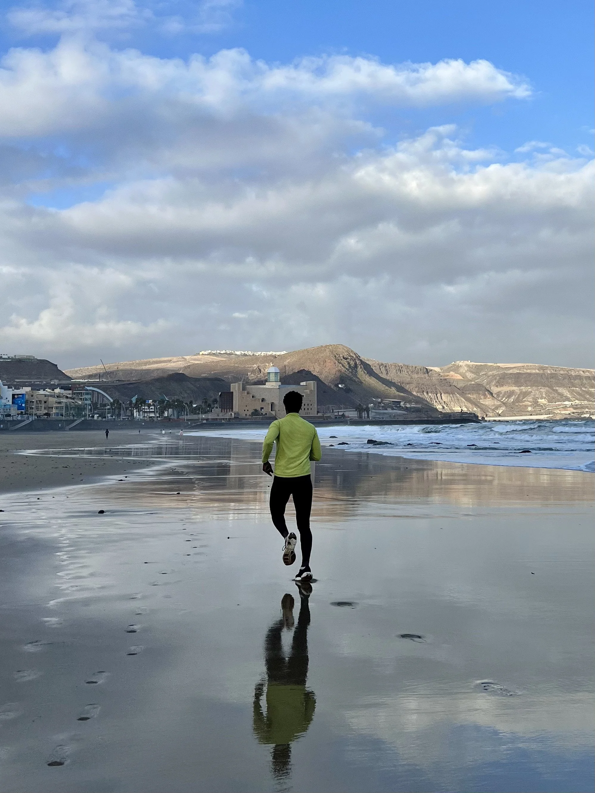 Deportista corriendo en la playa con la ciudad de fondo