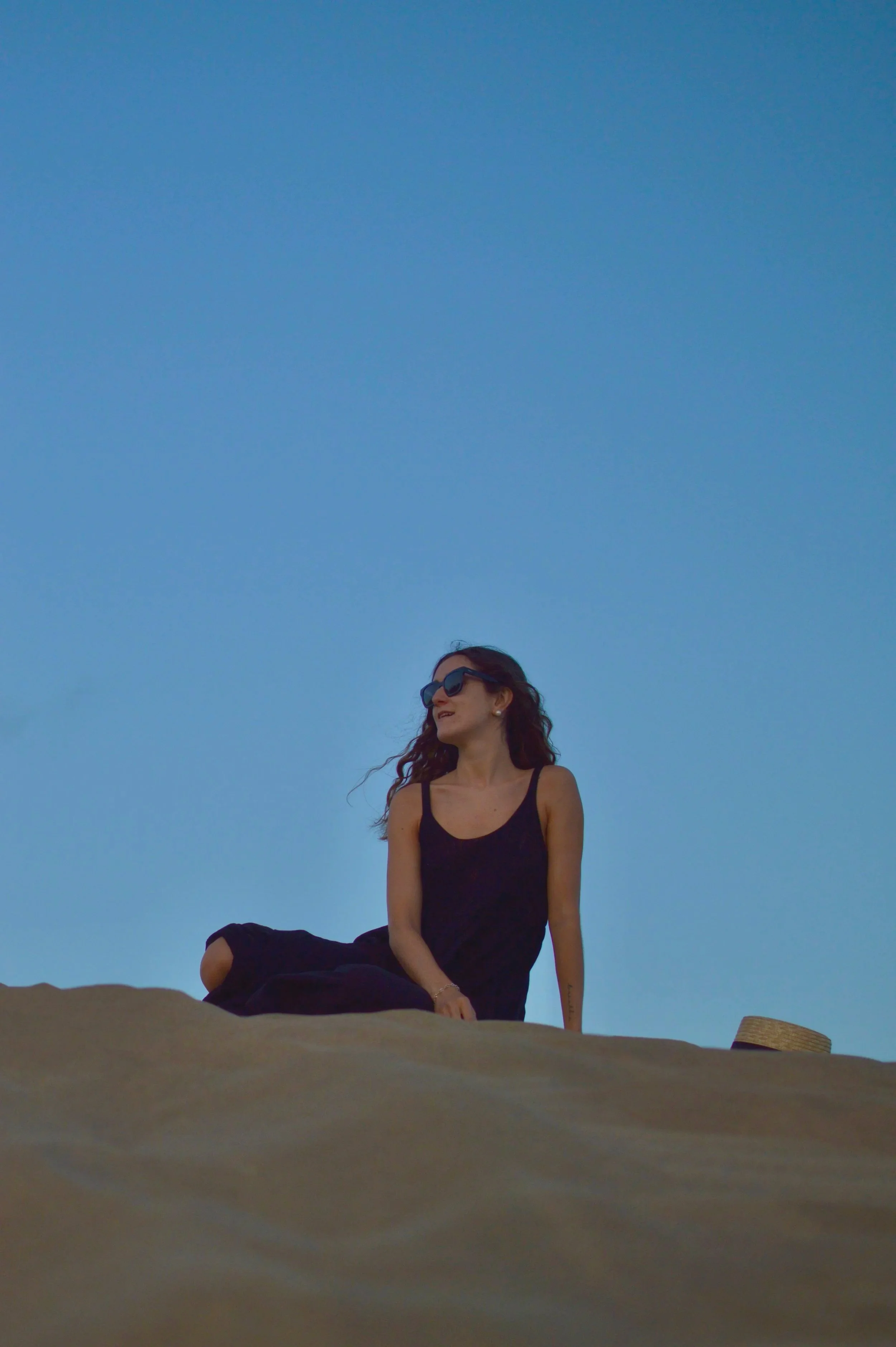 Chica posando en unas dunas de la playa con vestido negro y gafas