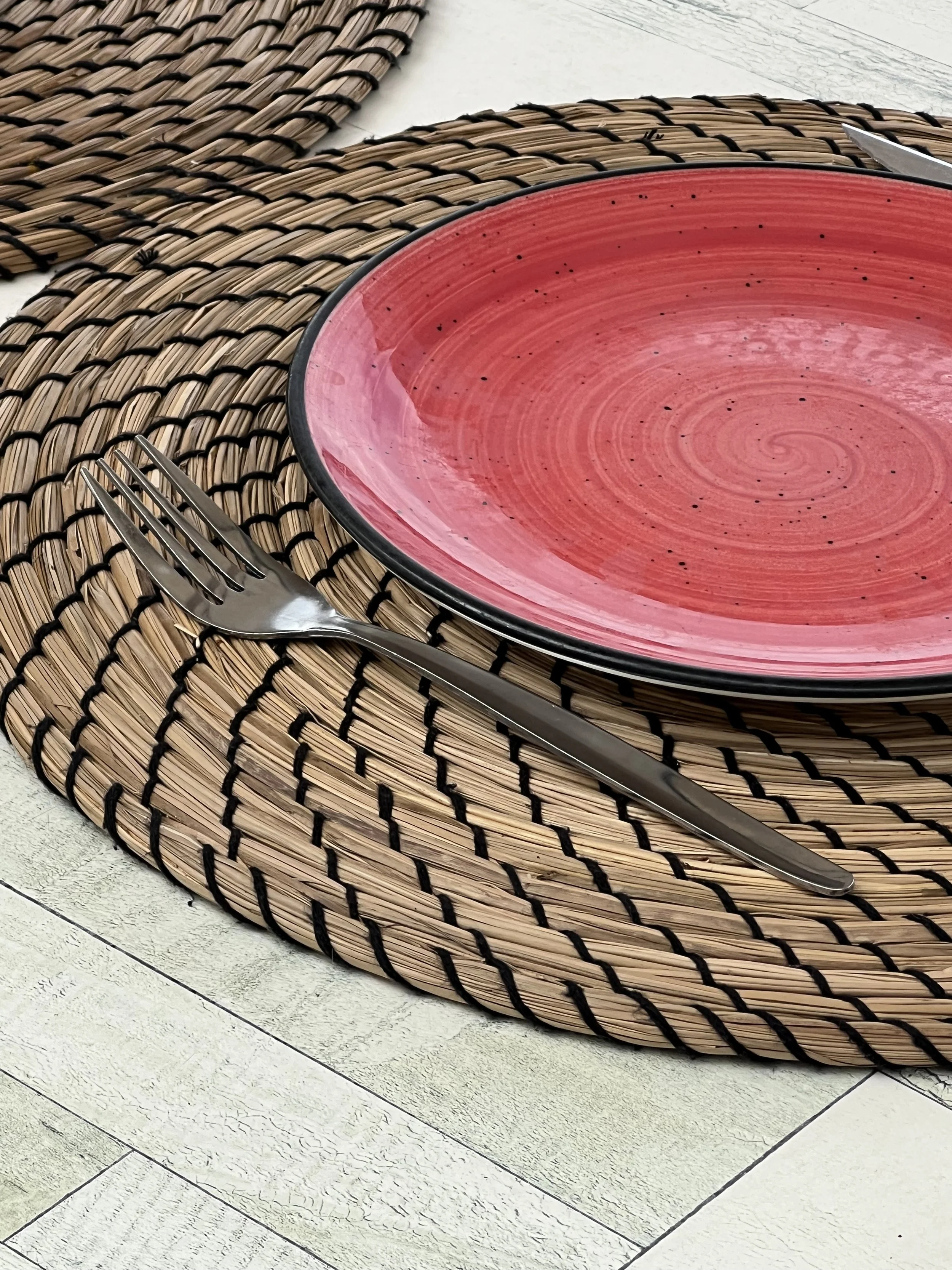 Plato rojo colocado sobre una mesa junto a un tenedor y mantel de mimbre