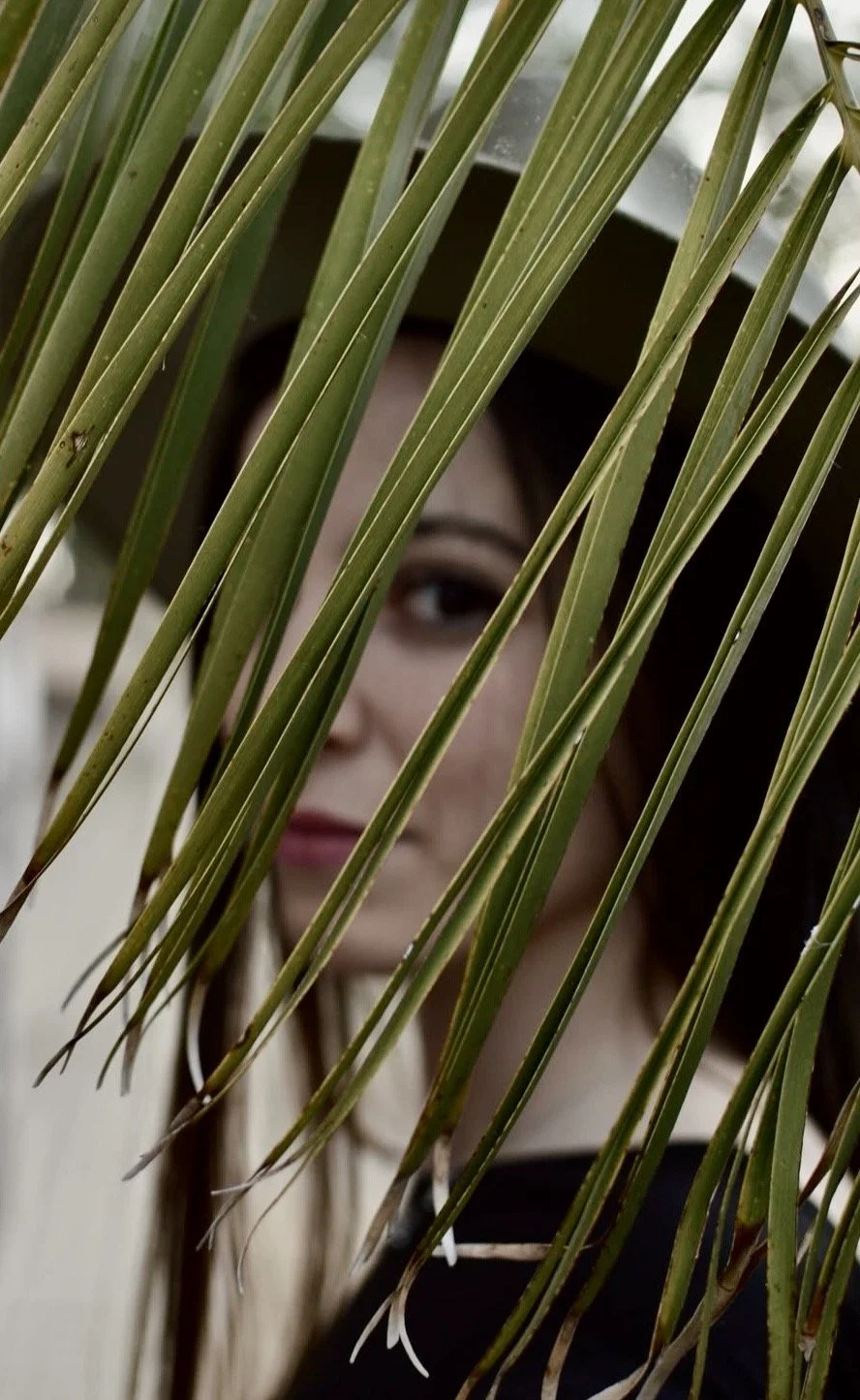 Mujer fotografiada detrás de las hojas de una palmera con un sombrero