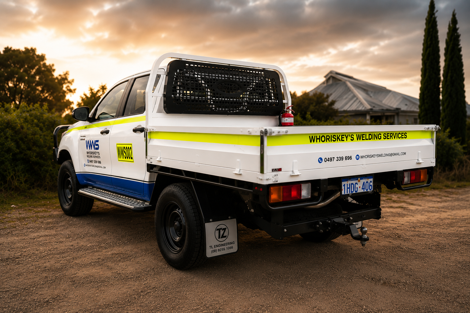 A white utility truck with yellow and blue markings, parked outdoors at sunset, labeled for Whoriskey's Welding Services, with contact info and a fire extinguisher in the truck bed.