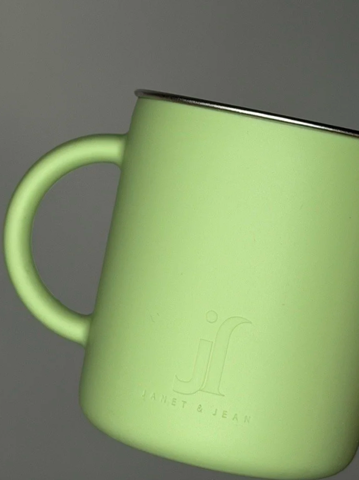 A light green metal mug with a handle and a logo for Janet & Jean, partially visible.