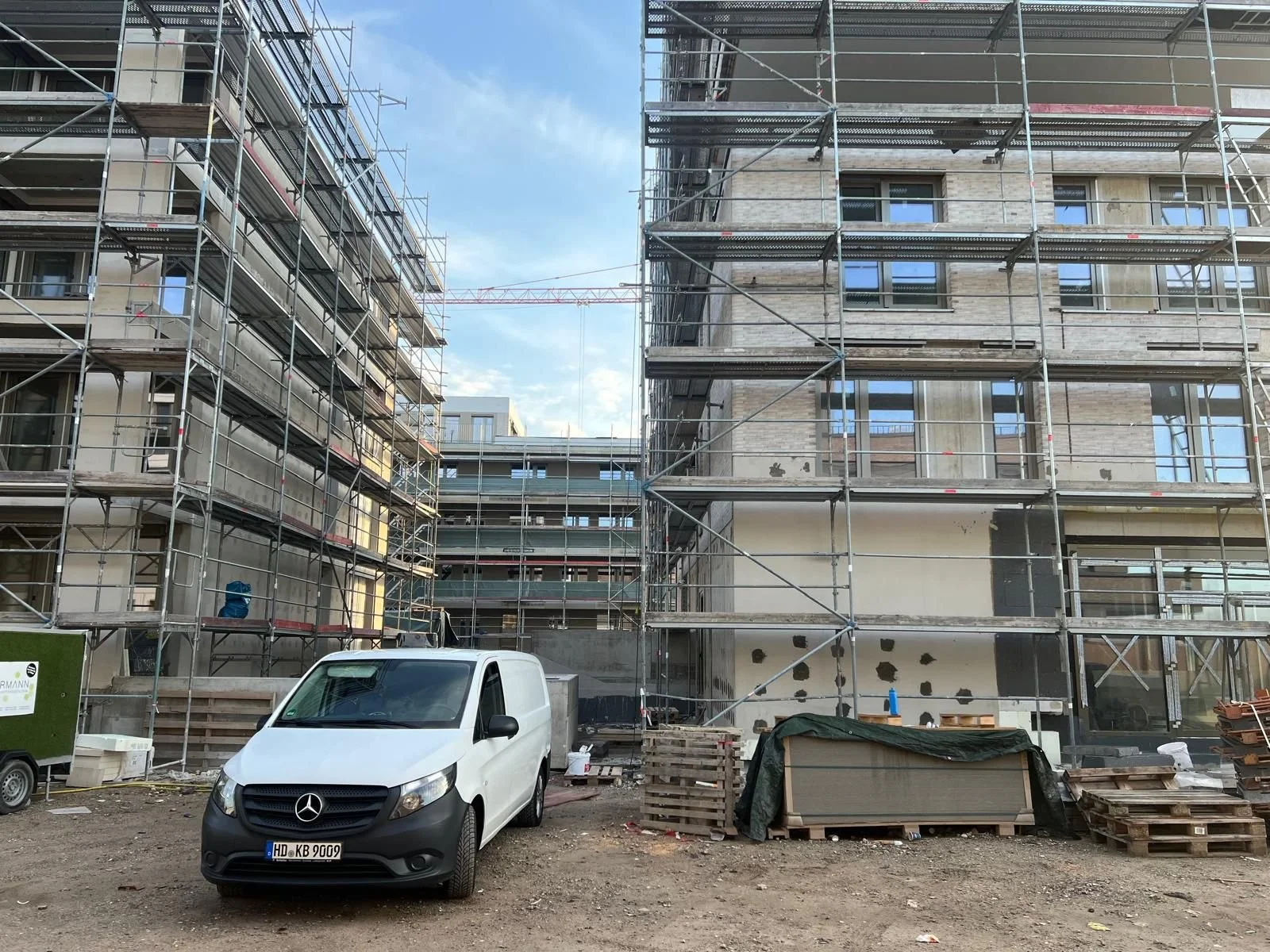 Baustelle mit zwei Gebäuden, die mit Gerüsten umgeben sind, und einem weißen Dienstwagen im Vordergrund.