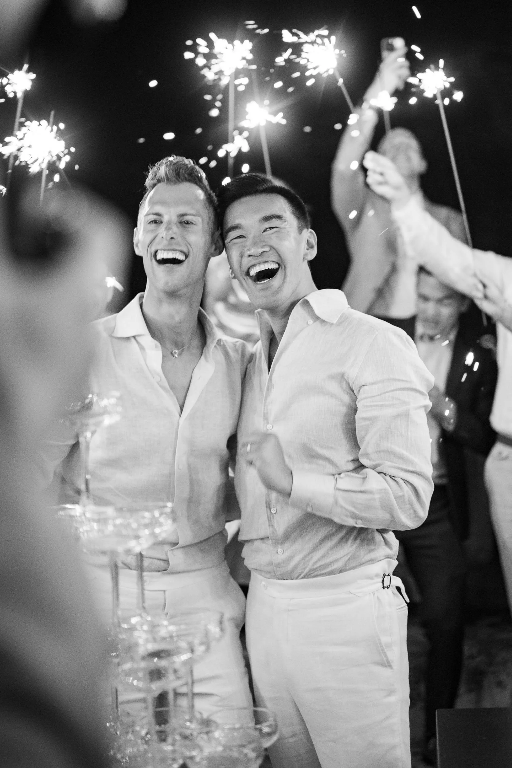 Two grooms celebrating with sparklers at a party, smiling and enjoying the moment at Forte da Cruz in Cascais, Portugal.