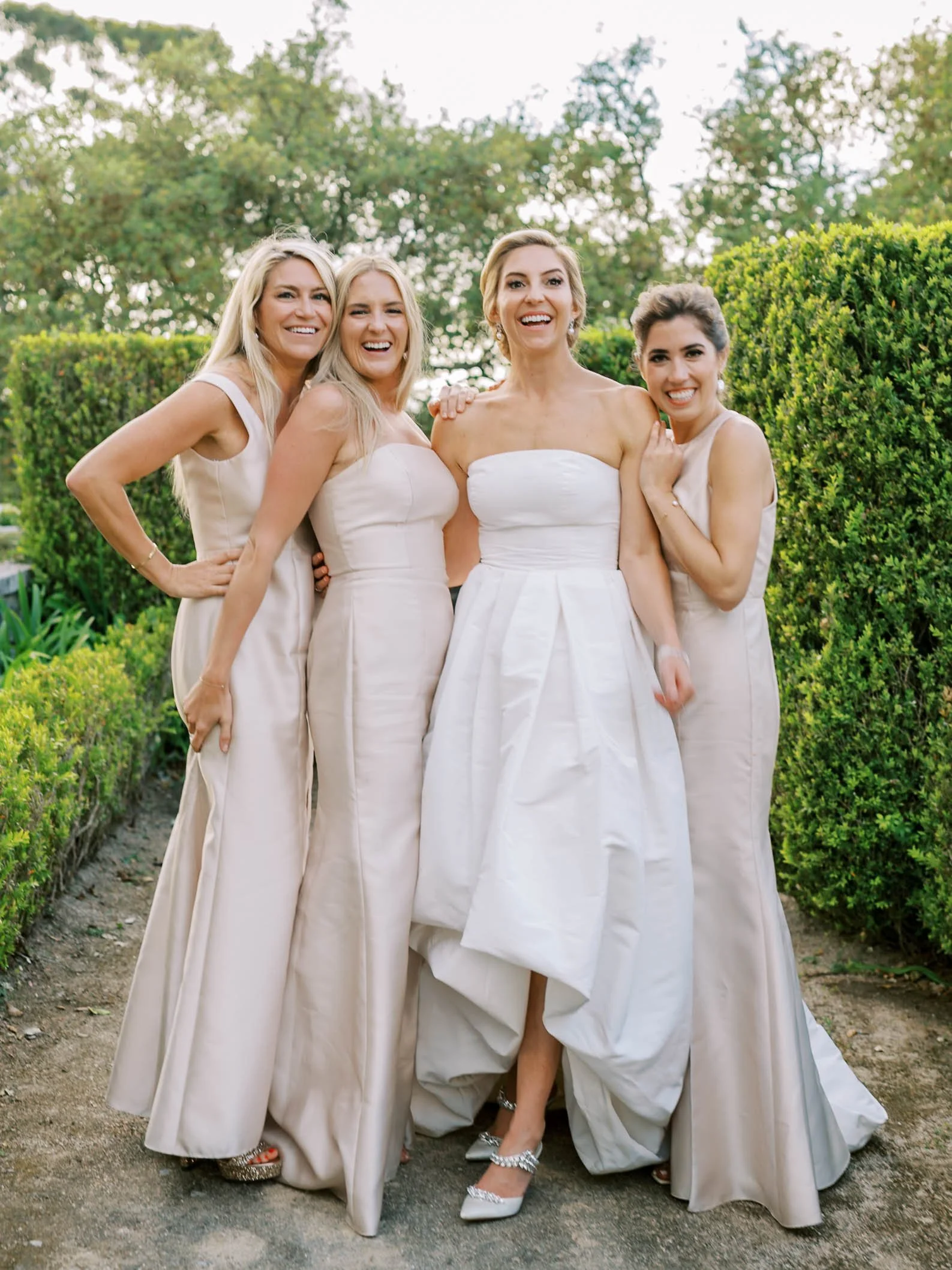 A bride in a white wedding dress standing with four bridesmaids also in white dresses, smiling outdoors among green bushes and trees at Palácio de Seteais in Sintra, Portugal