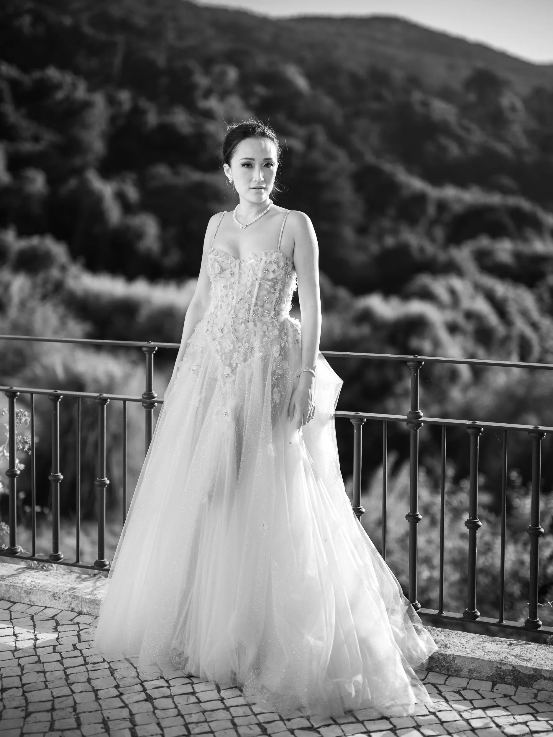 A bride standing outdoors on a cobblestone pathway with a mountain landscape in the background in Sintra.