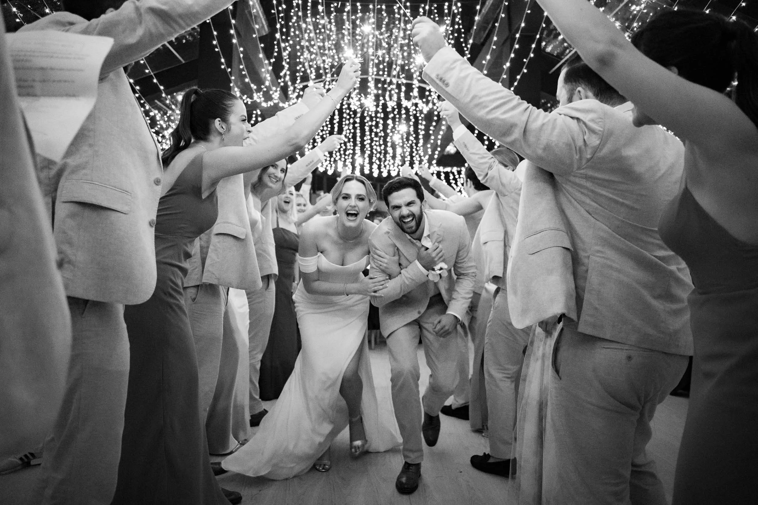 A wedding celebration with a bride and groom dancing through a tunnel of friends or family under string lights at Amanpuri Phuket in Thailand