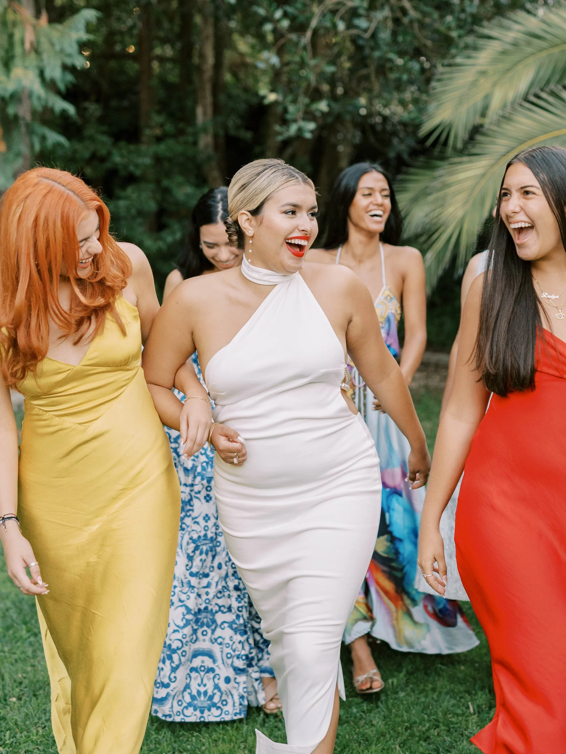 A bride and bridesmaids dressed in colorful dresses enjoying a conversation outdoors in a green garden in Sintra
